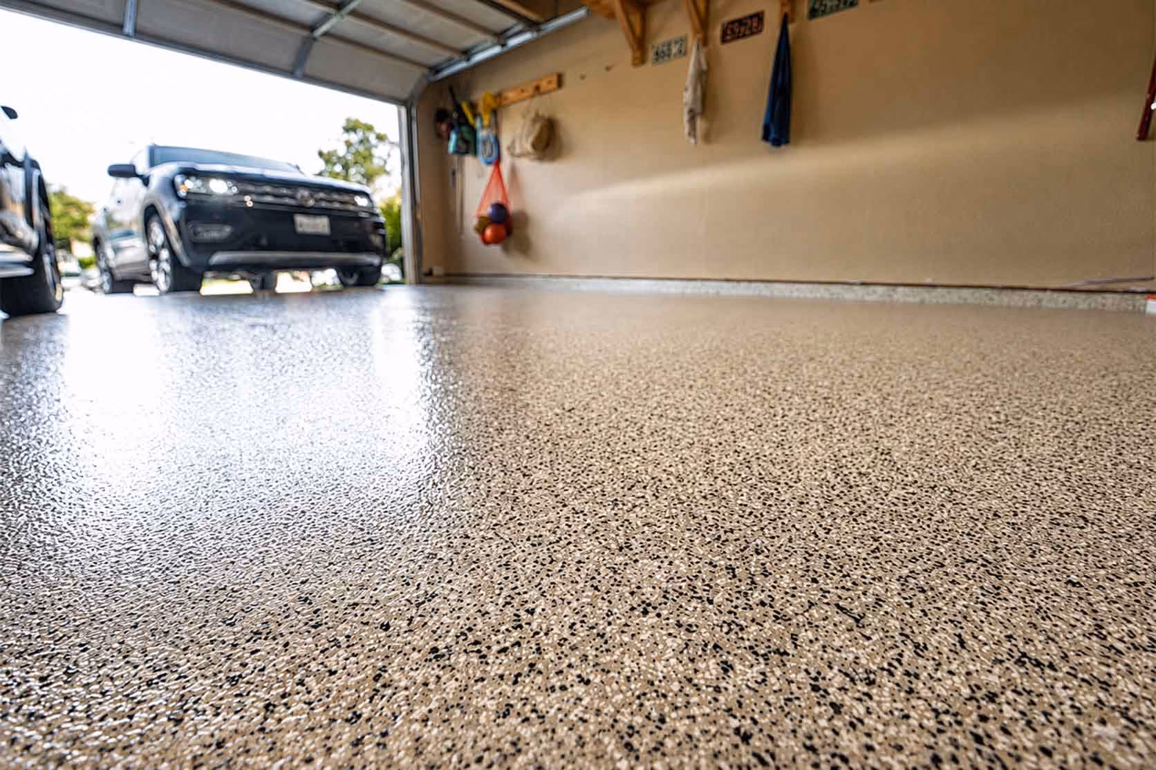 Glossy speckled epoxy garage floor with a black SUV parked near the open garage door.