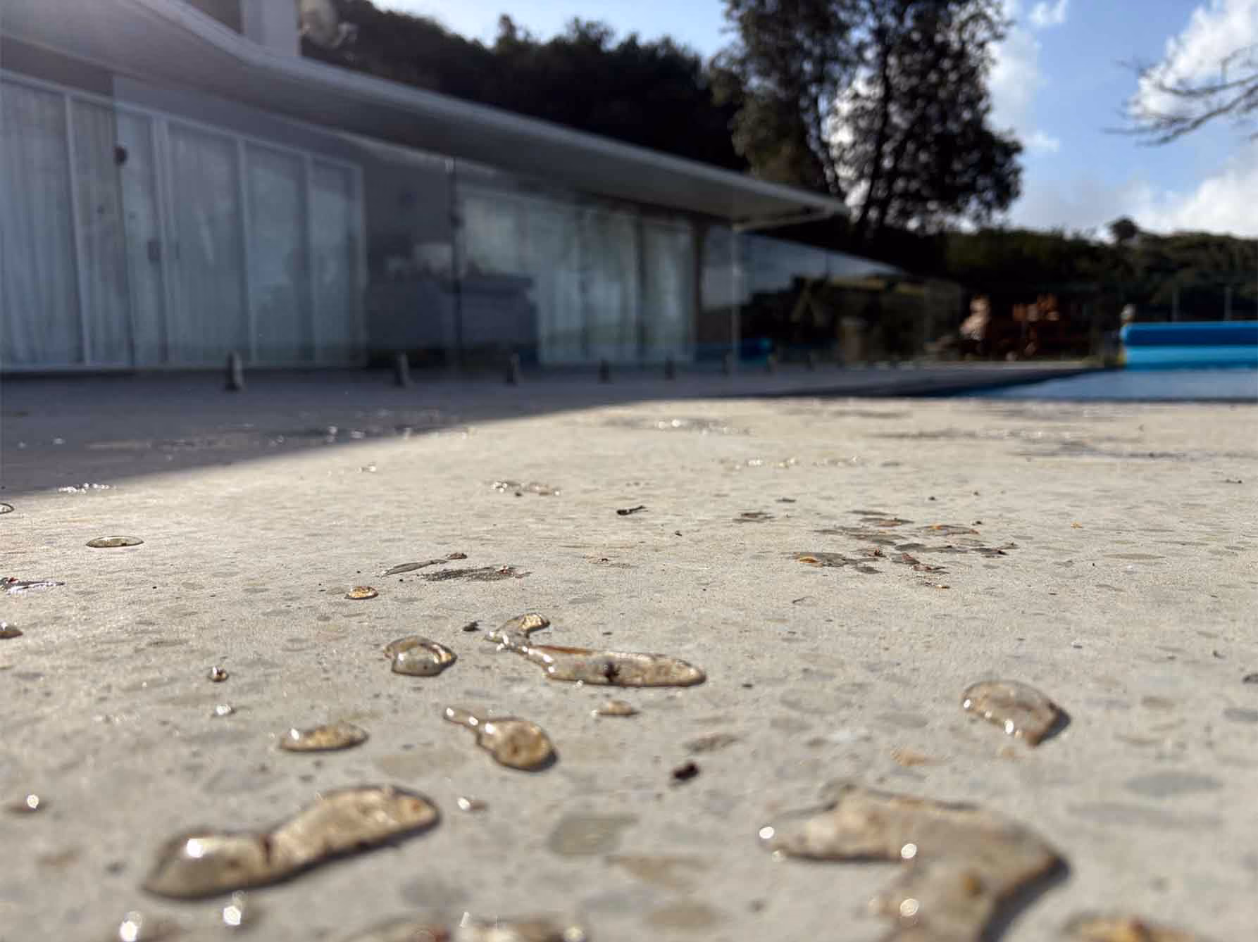 Water droplets on a concrete pool deck surface with a house and trees in the background.