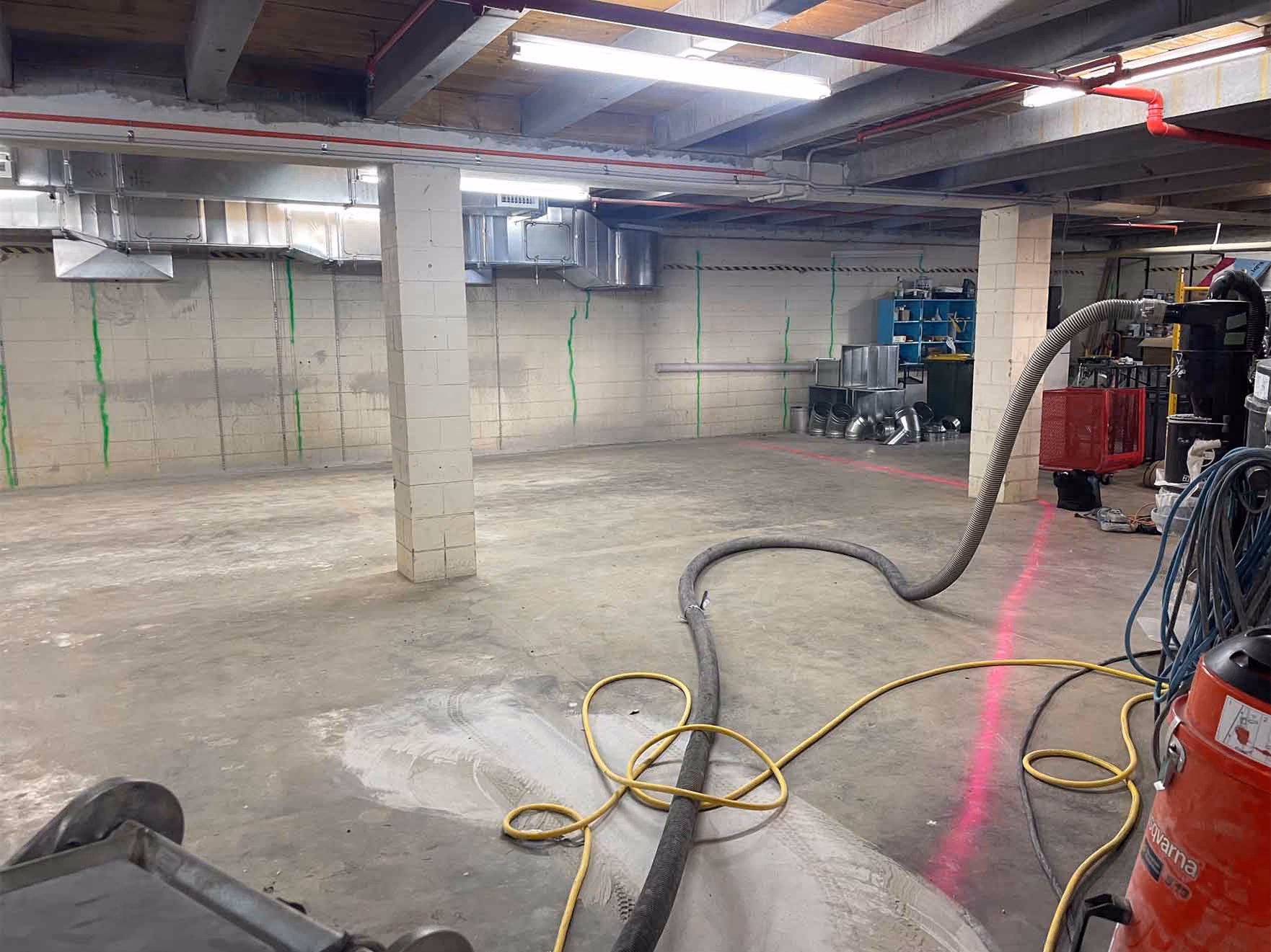 Empty spacious basement with concrete floor, ventilation ducts, pillars, and coiled hoses on the floor.
