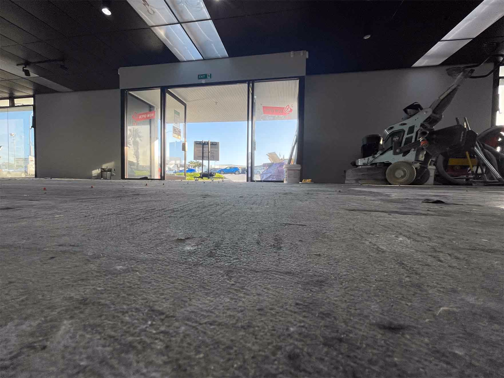 Interior of a commercial space under renovation with bare concrete floor and floor polishing equipment.