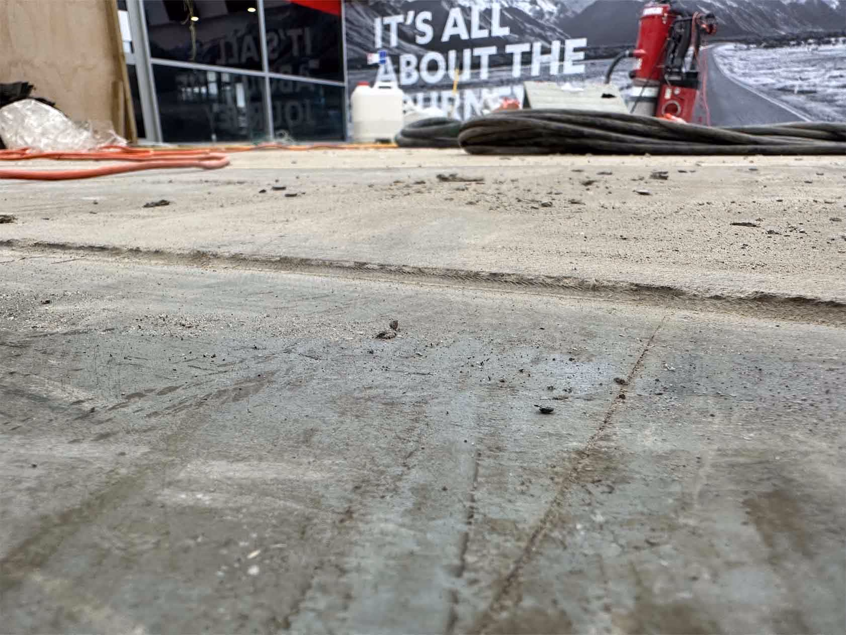 Close-up of concrete floor with visible cracks and construction equipment in the background.