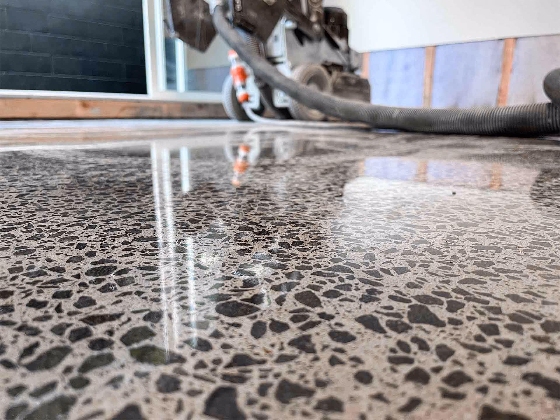 Close-up of a polished terrazzo floor with black and gray stone chips reflected in light.