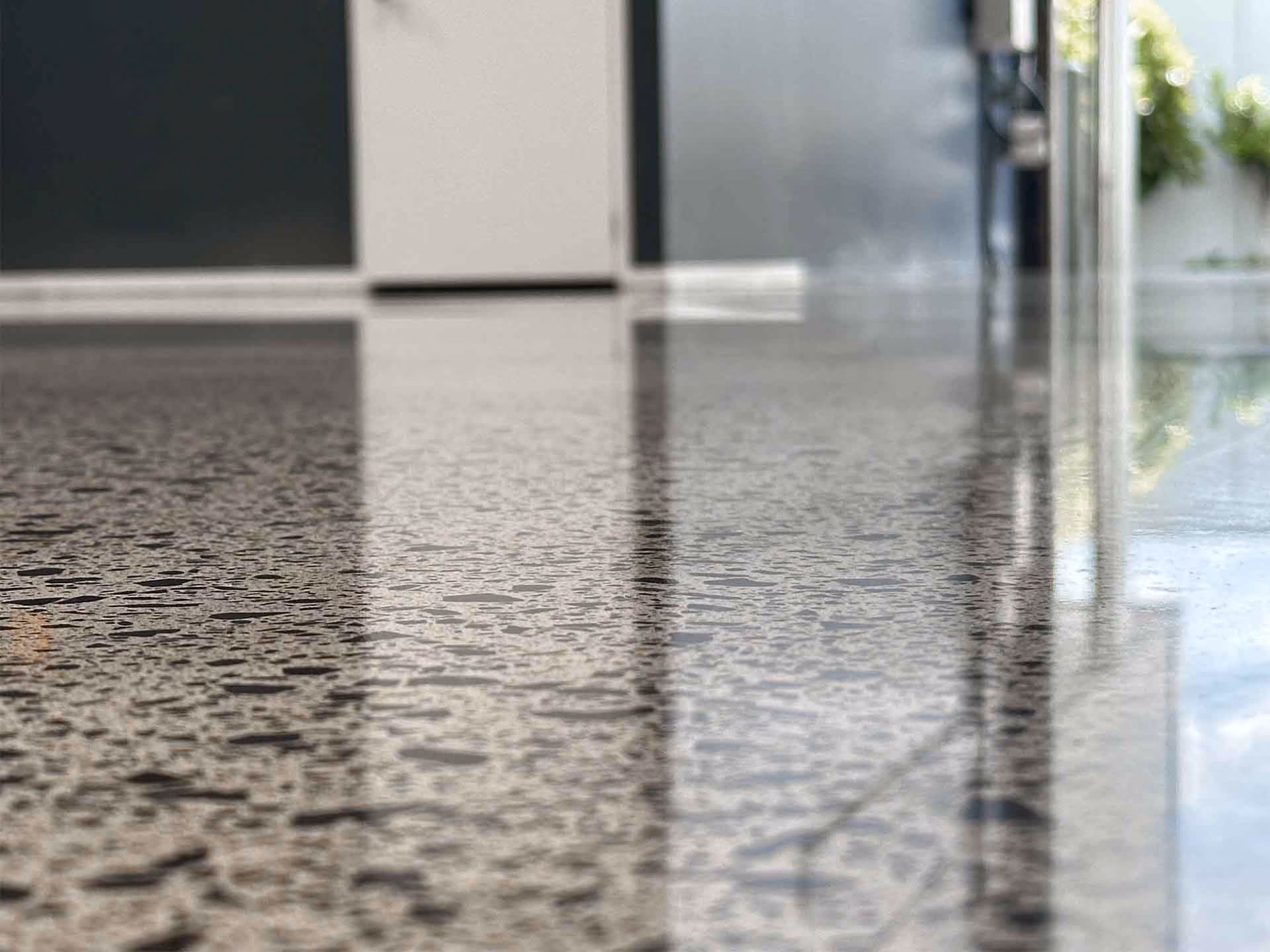 Close-up of a polished terrazzo floor reflecting a modern interior with doors and plants.