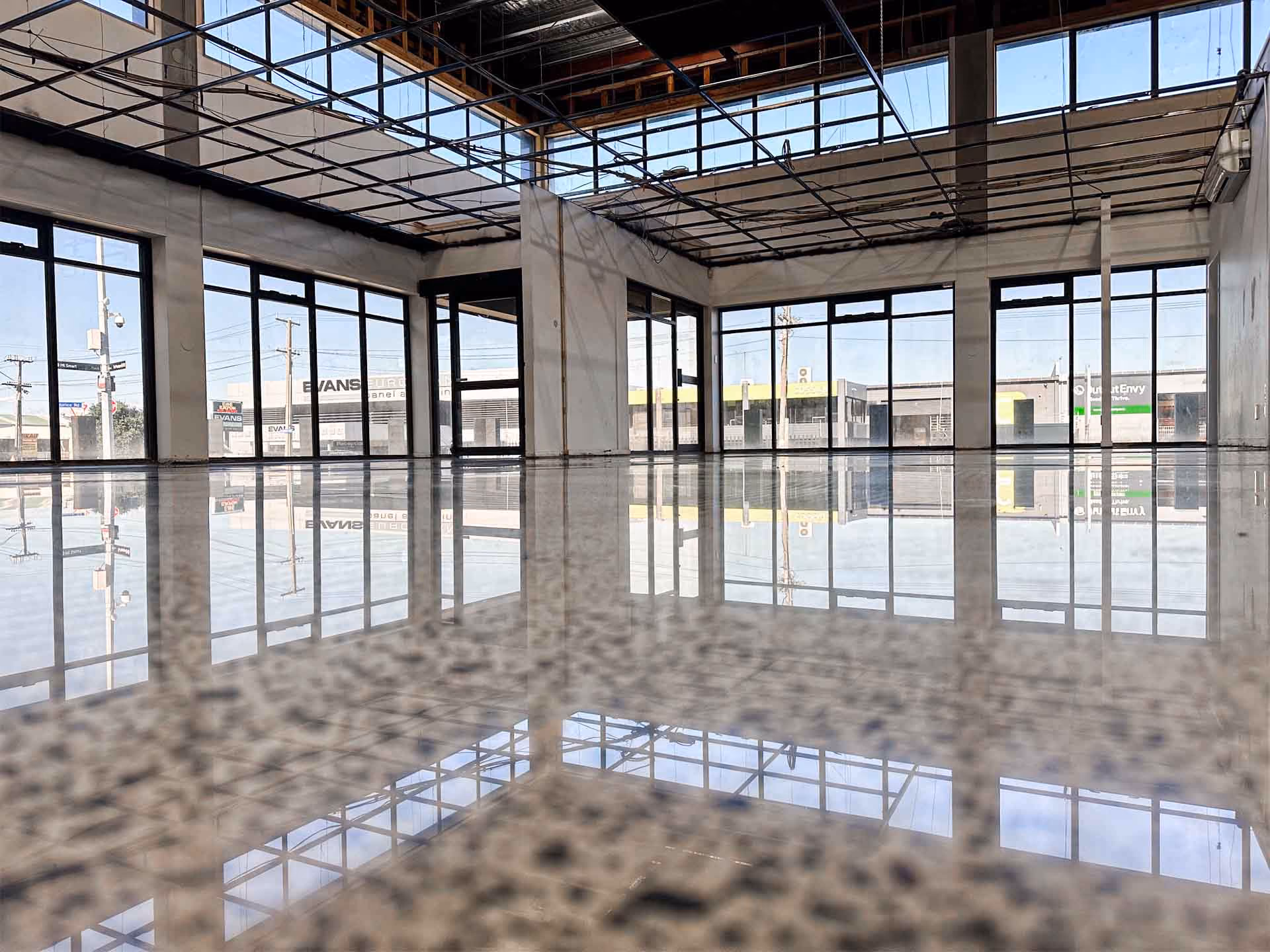 Empty commercial space with polished floor reflecting large windows and ceiling framework.