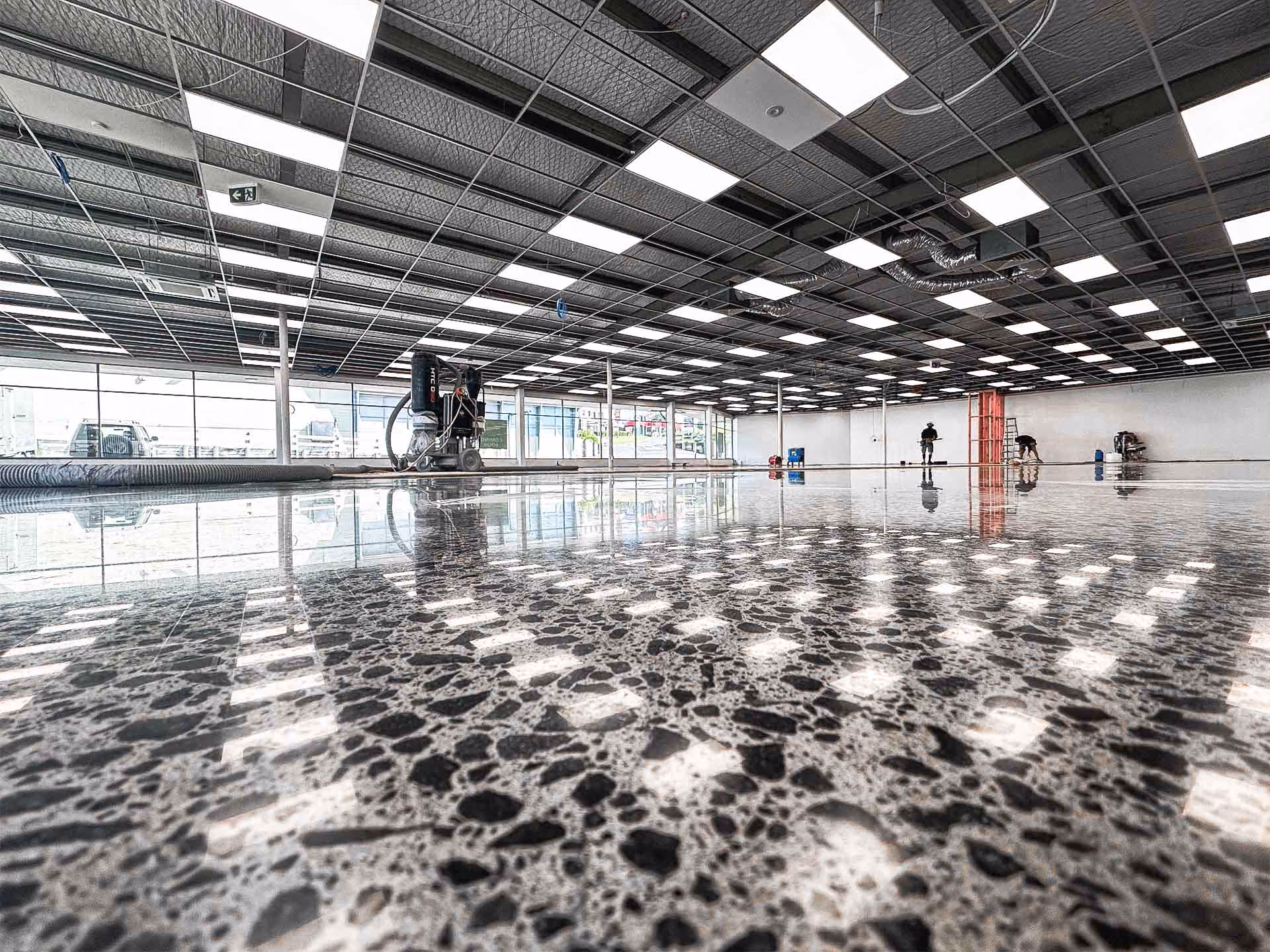 Polished concrete floor in large commercial space with workers and equipment under a grid ceiling.