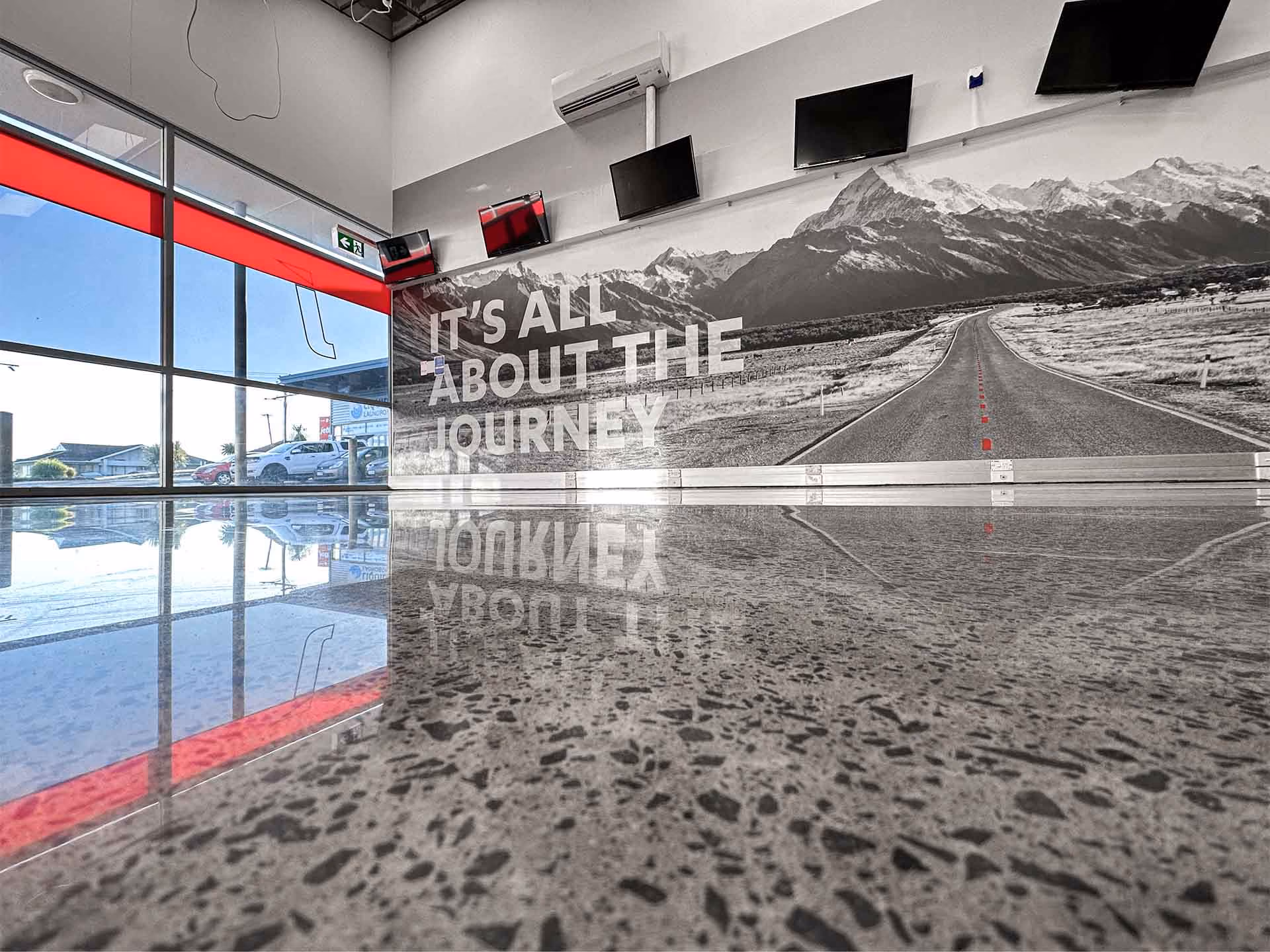 Gym wall mural with road and mountains and text: It's all about the journey, reflected on polished floor.