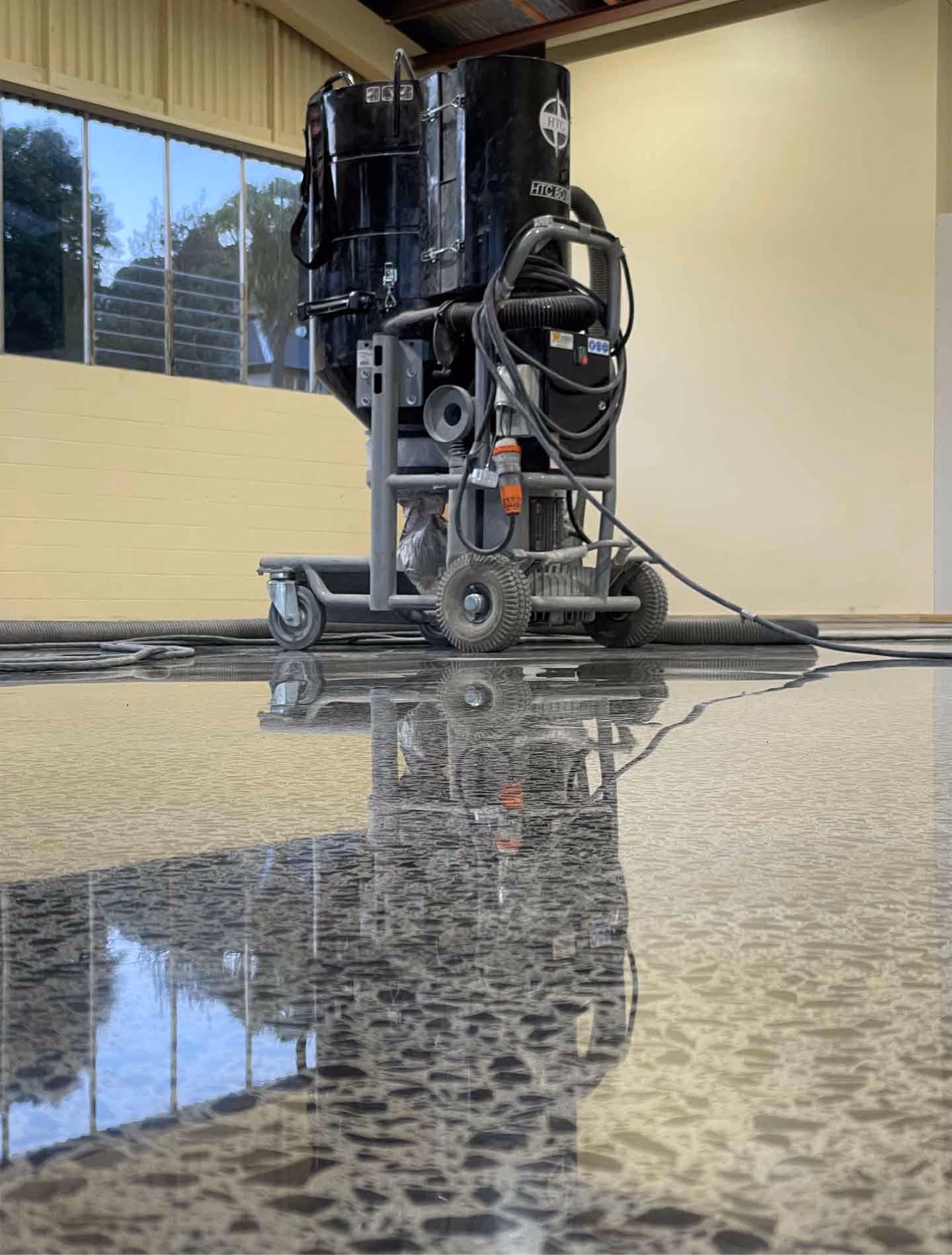 Black industrial floor machine on wheels reflecting on freshly polished concrete floor.