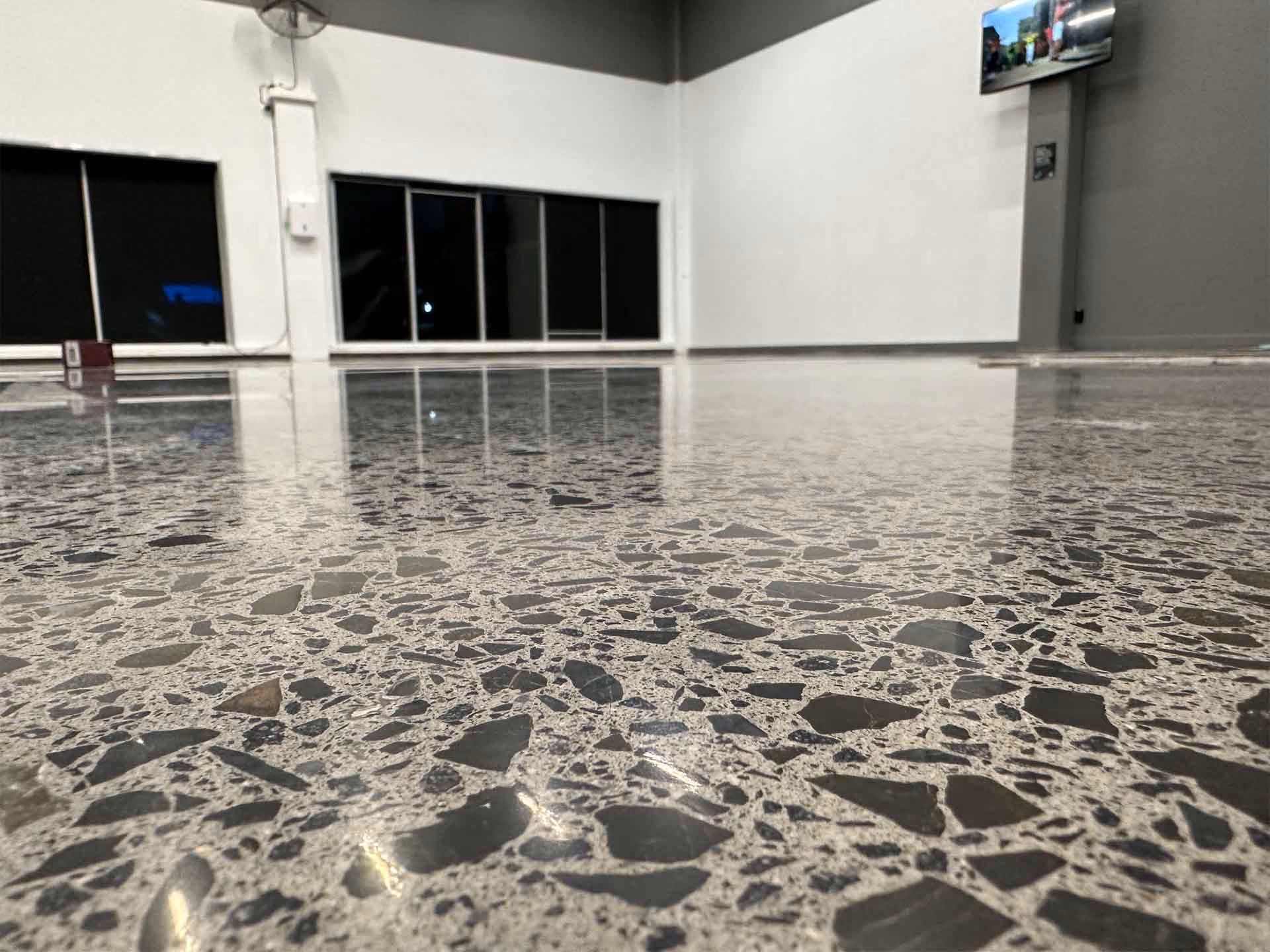 Close-up of polished terrazzo floor inside a large, mostly empty room with white walls and black windows.
