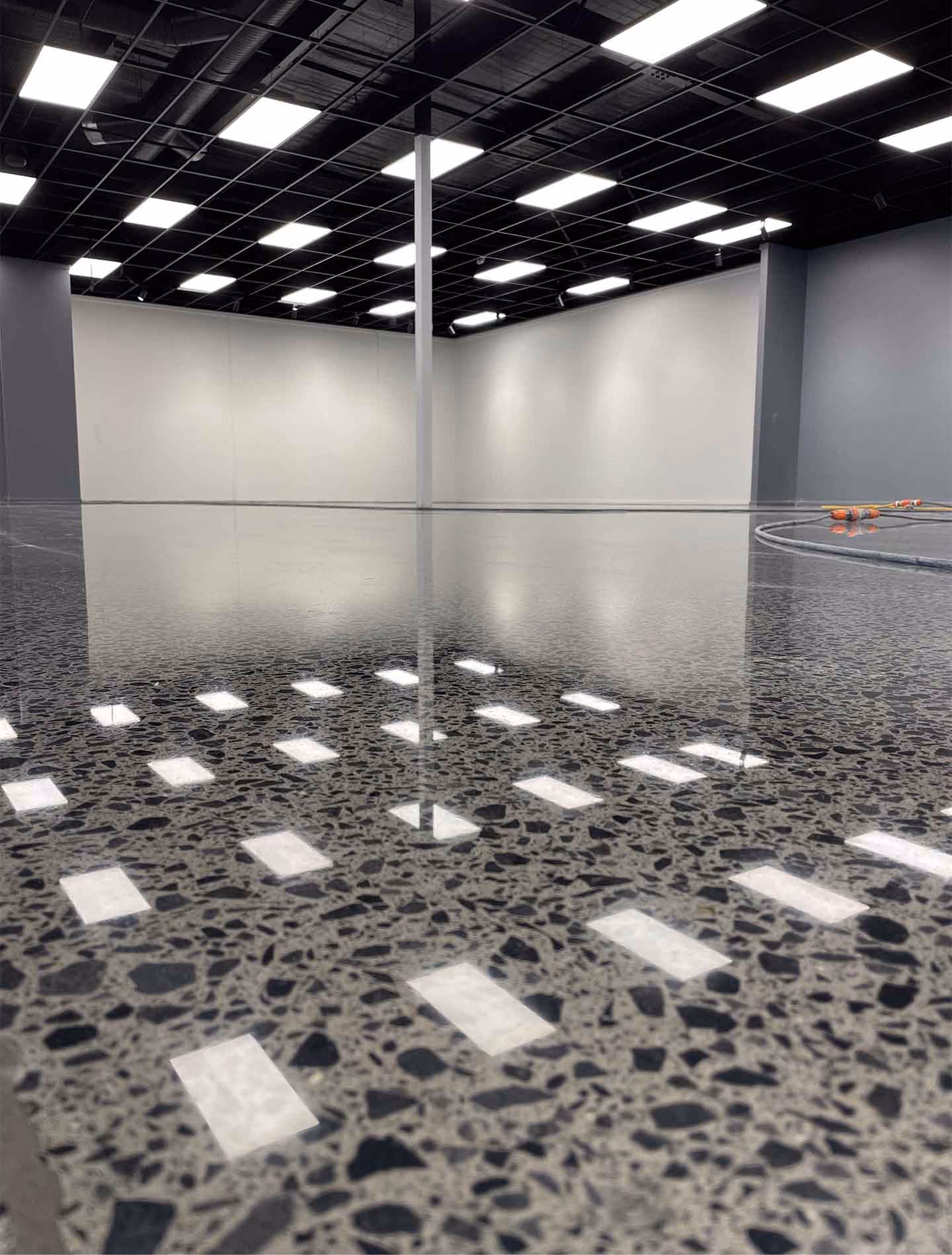 Polished terrazzo floor reflecting ceiling lights in an empty industrial space with white and gray walls.
