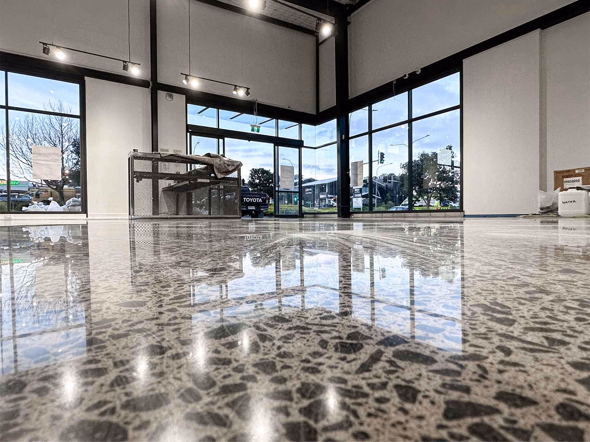 Polished concrete floor reflecting large windows showing a street view with cars and trees.