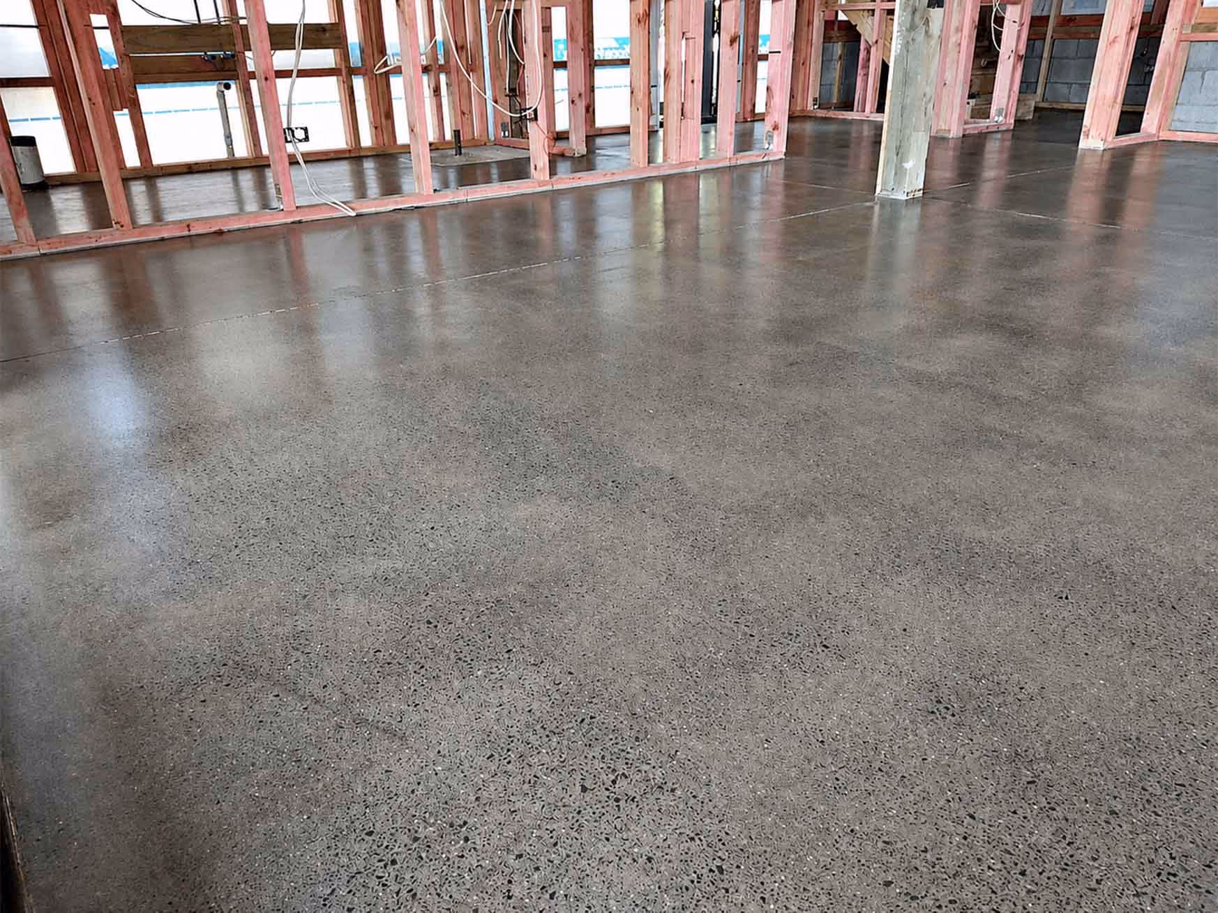 Polished concrete floor in a building under construction with exposed wooden framing and wiring.