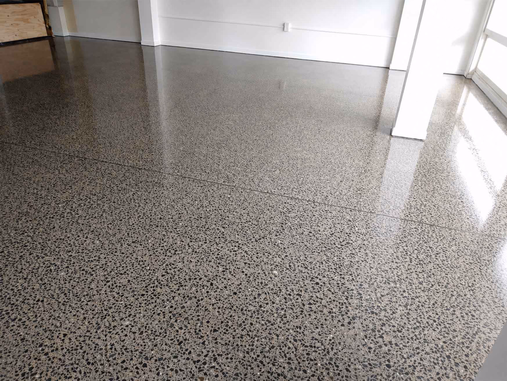 Polished terrazzo floor with a glossy finish reflecting light in an empty room with white walls.