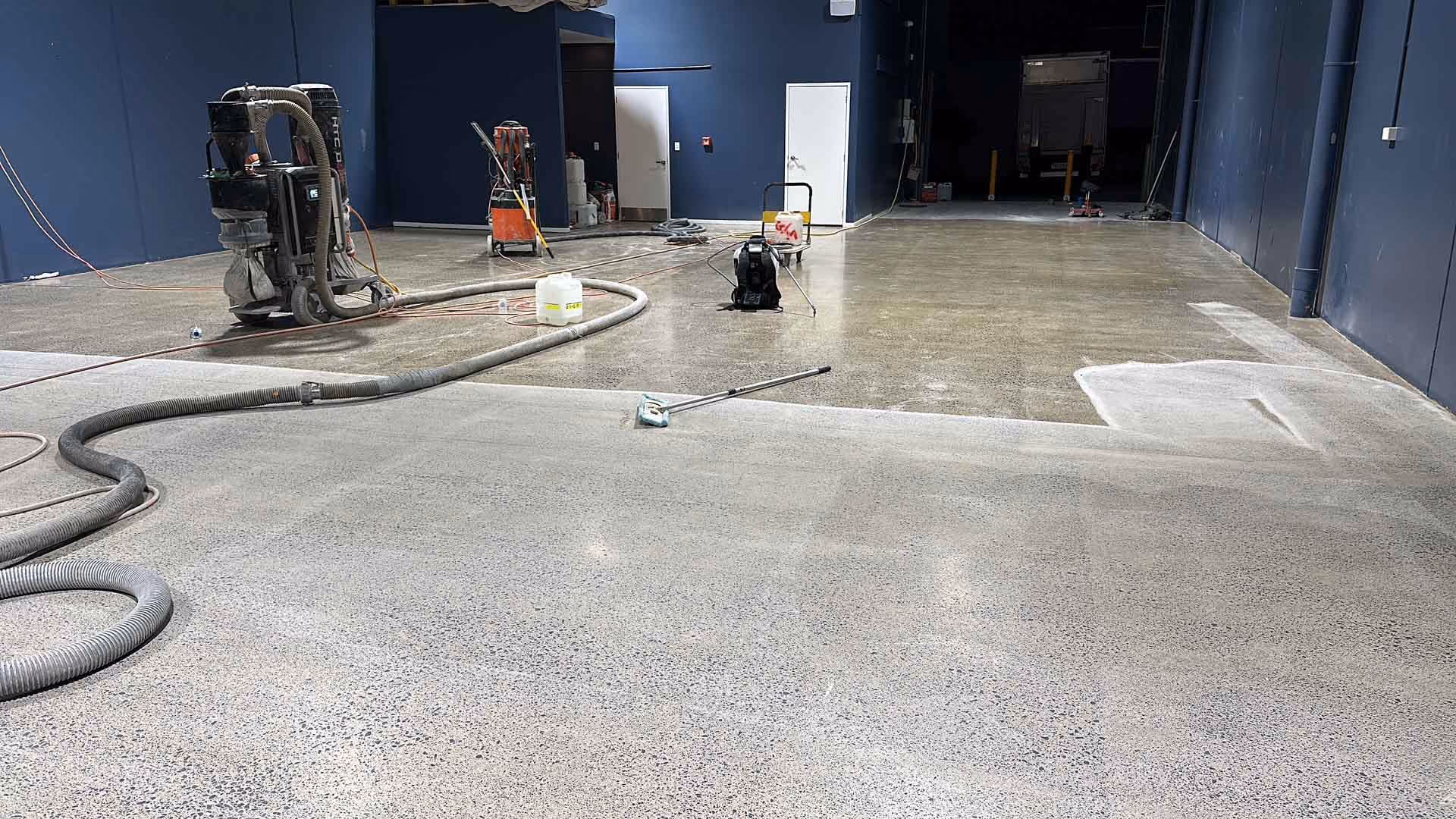 Indoor construction site with polished concrete floor and floor cleaning equipment and hoses.