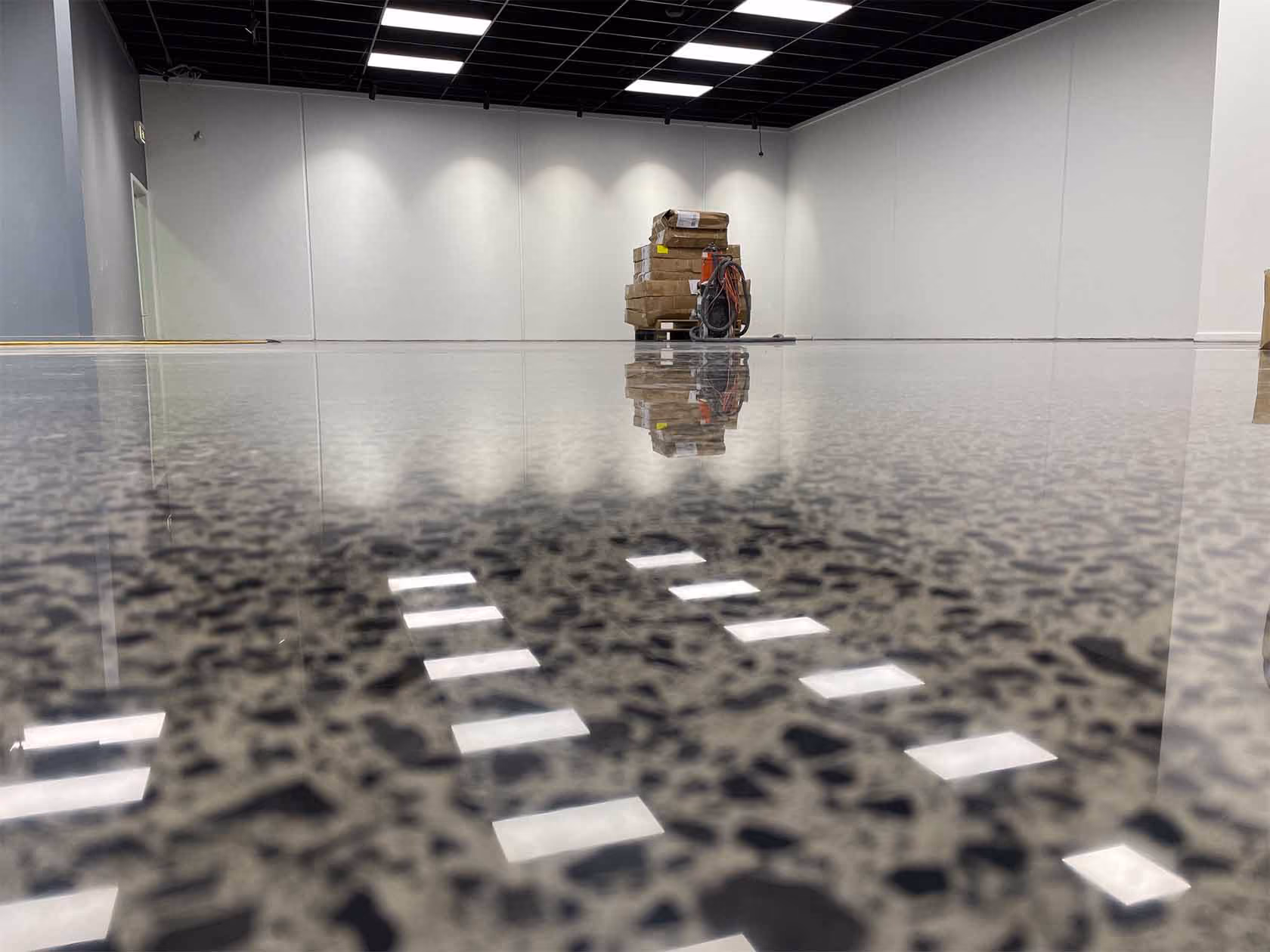 Polished terrazzo floor reflecting ceiling lights and stacked boxes in an empty room.