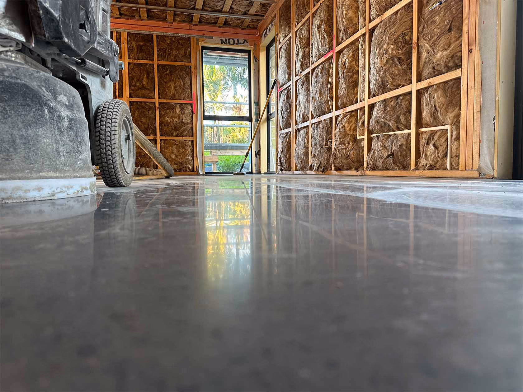 Low-angle view of a polished concrete floor in a room under construction with exposed insulated walls.
