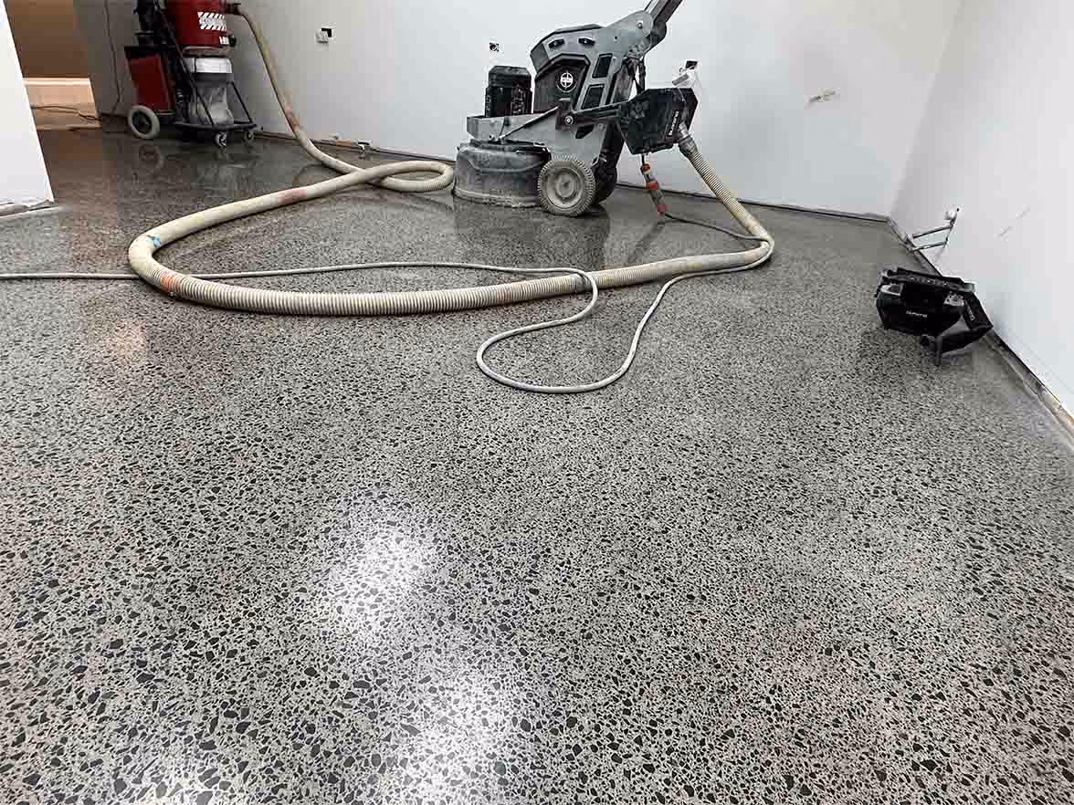 Polished concrete floor with floor grinding machine and vacuum hose in an empty room with white walls.