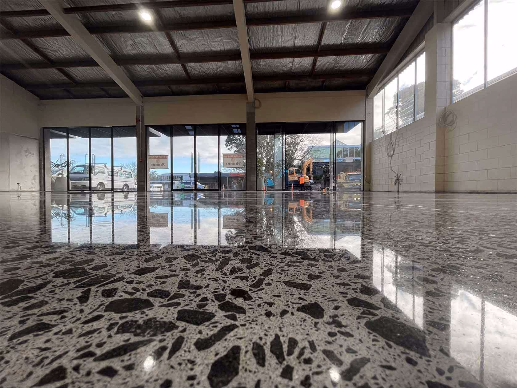 Polished concrete floor reflecting garage doors and vehicles outside a warehouse.