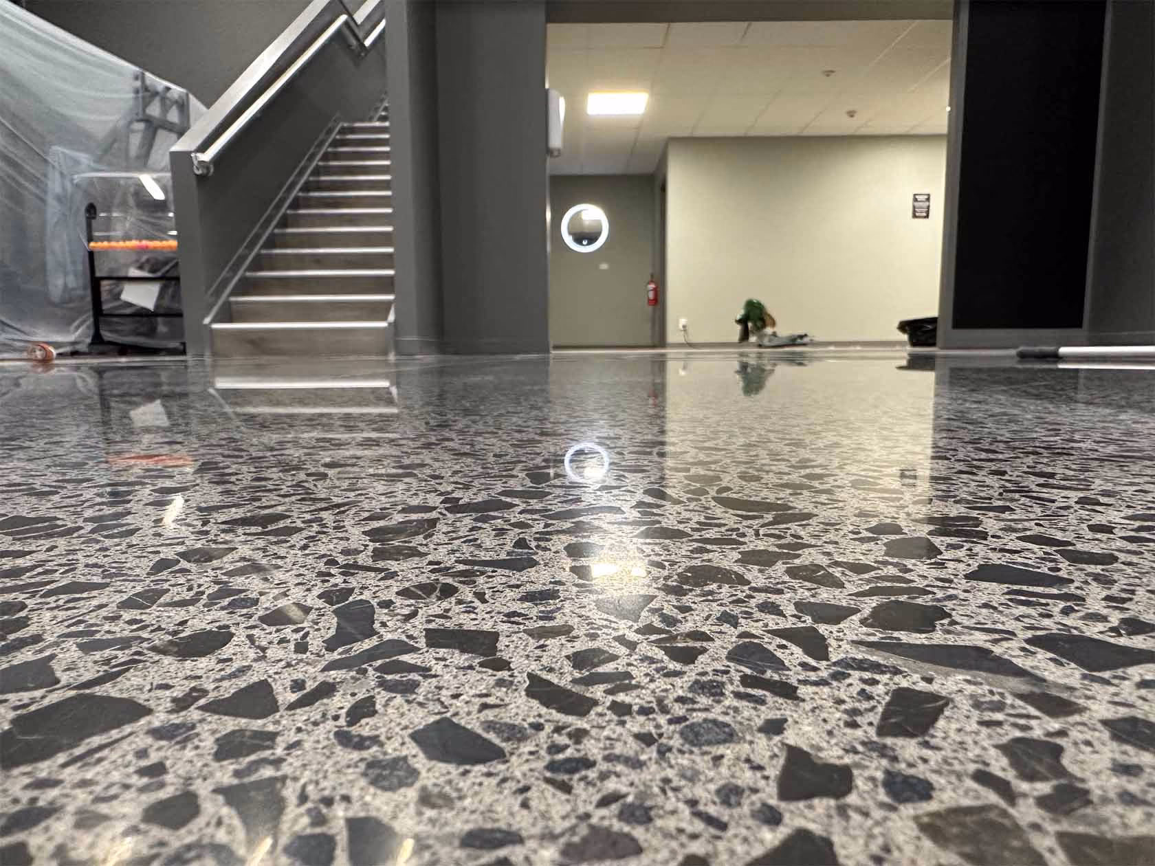 Polished terrazzo floor with black and white chips reflecting light in an indoor space with stairs.