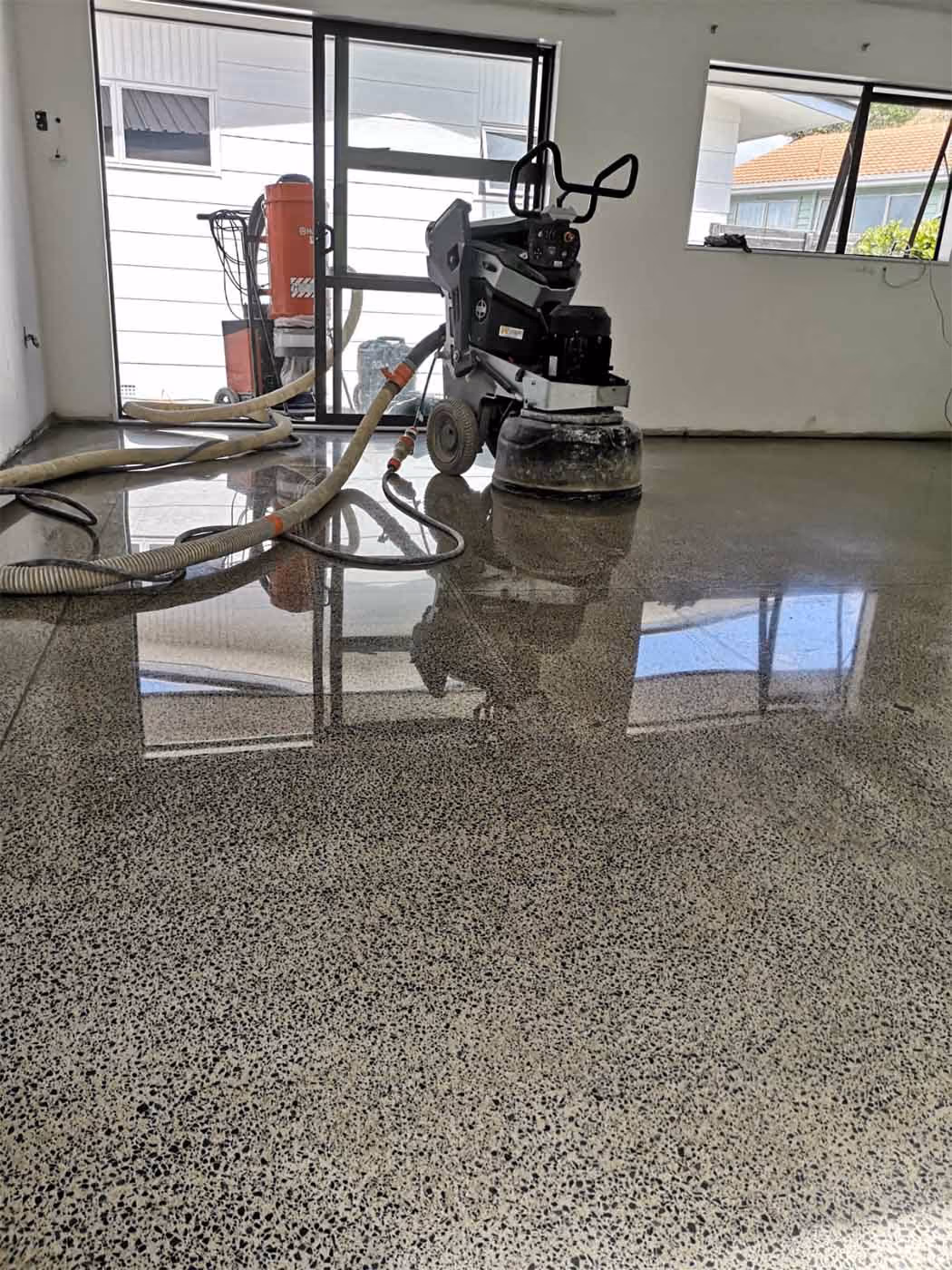 Polished concrete floor inside a room with floor grinding machine and vacuum equipment.