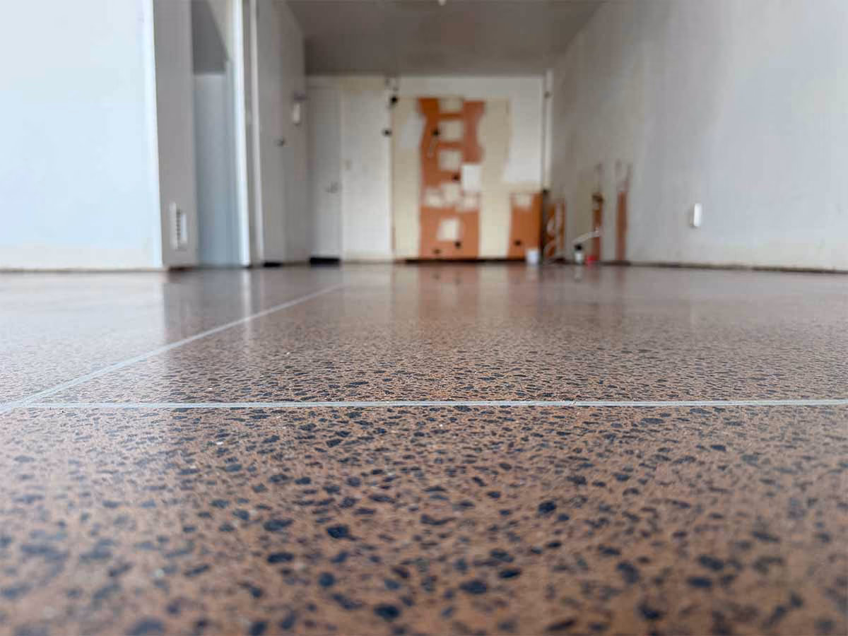 Close-up of brown speckled tile floor in an empty room with white walls and an open doorway.
