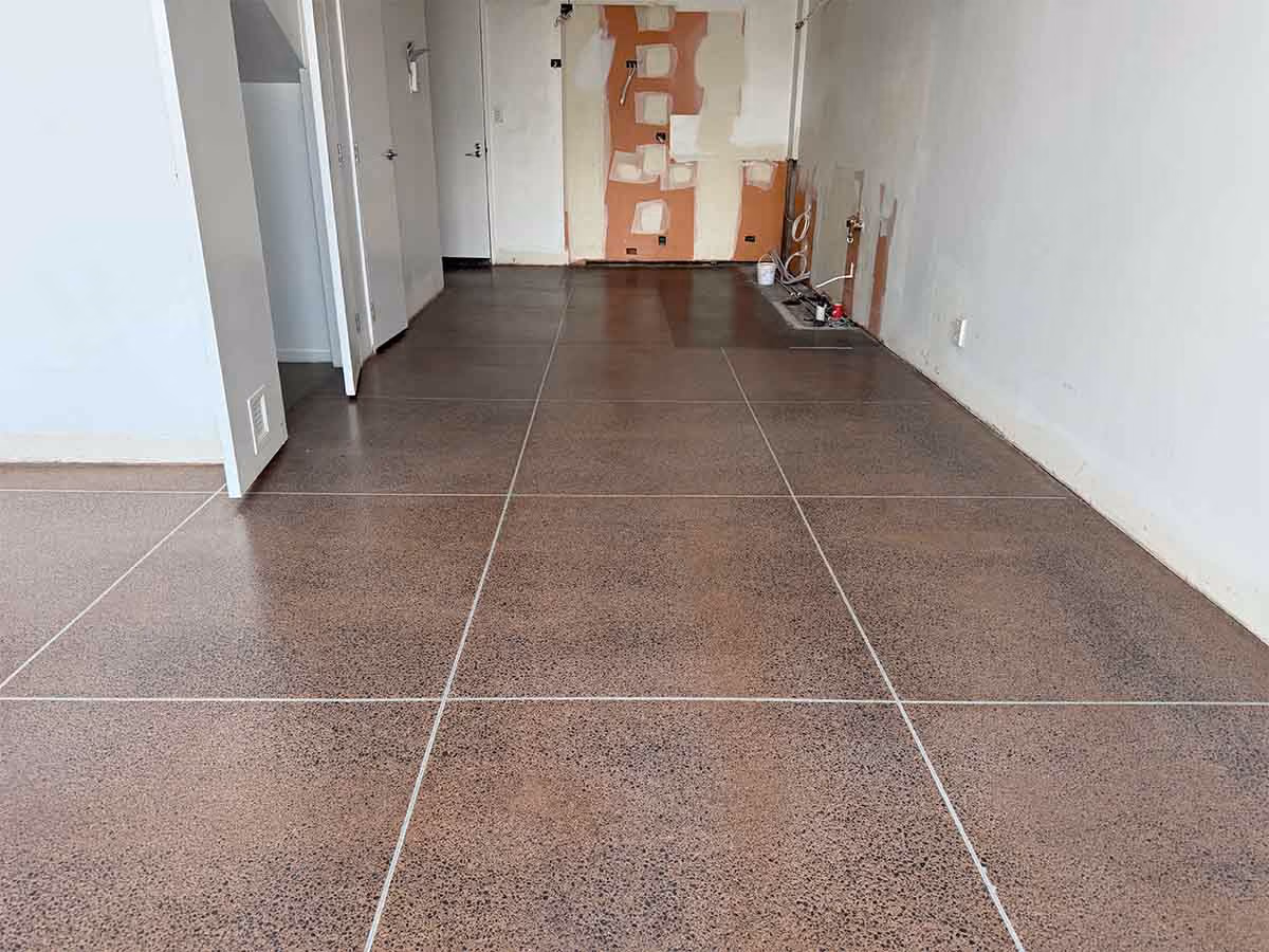Empty room with polished brown tiled floor and white walls, some wall patches visible in the back.