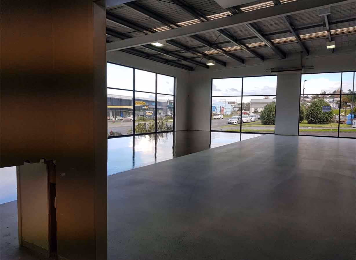 Empty commercial space with polished concrete floors, large windows, and exposed ceiling beams.