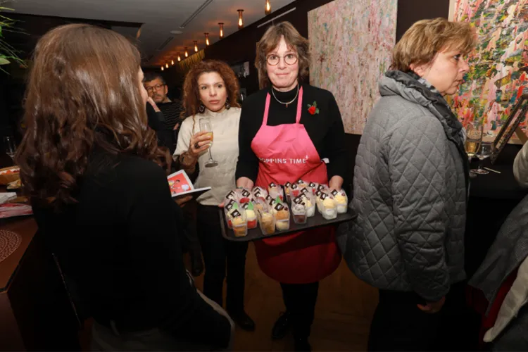 Femme en tablier rose portant un plateau de desserts lors d'un événement social en intérieur.