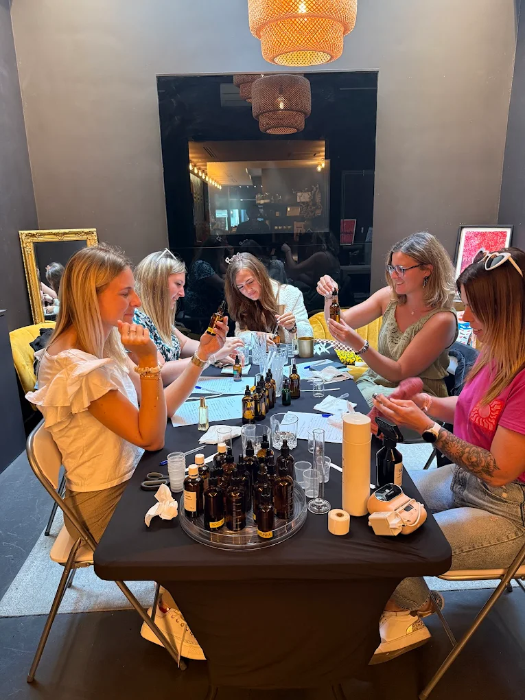 Cinq femmes assises à une table noire, manipulant de petites bouteilles en verre ambré dans un enterrement de vie de jeune fille.