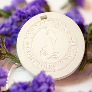 Un disque de parfum Les Nouveaux Comptoirs Olfactifs entouré de fleurs violettes au format carré