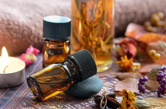 Deux petites bouteilles en verre ambré pour huiles essentielles avec une bougie allumée et des plantes sèches.