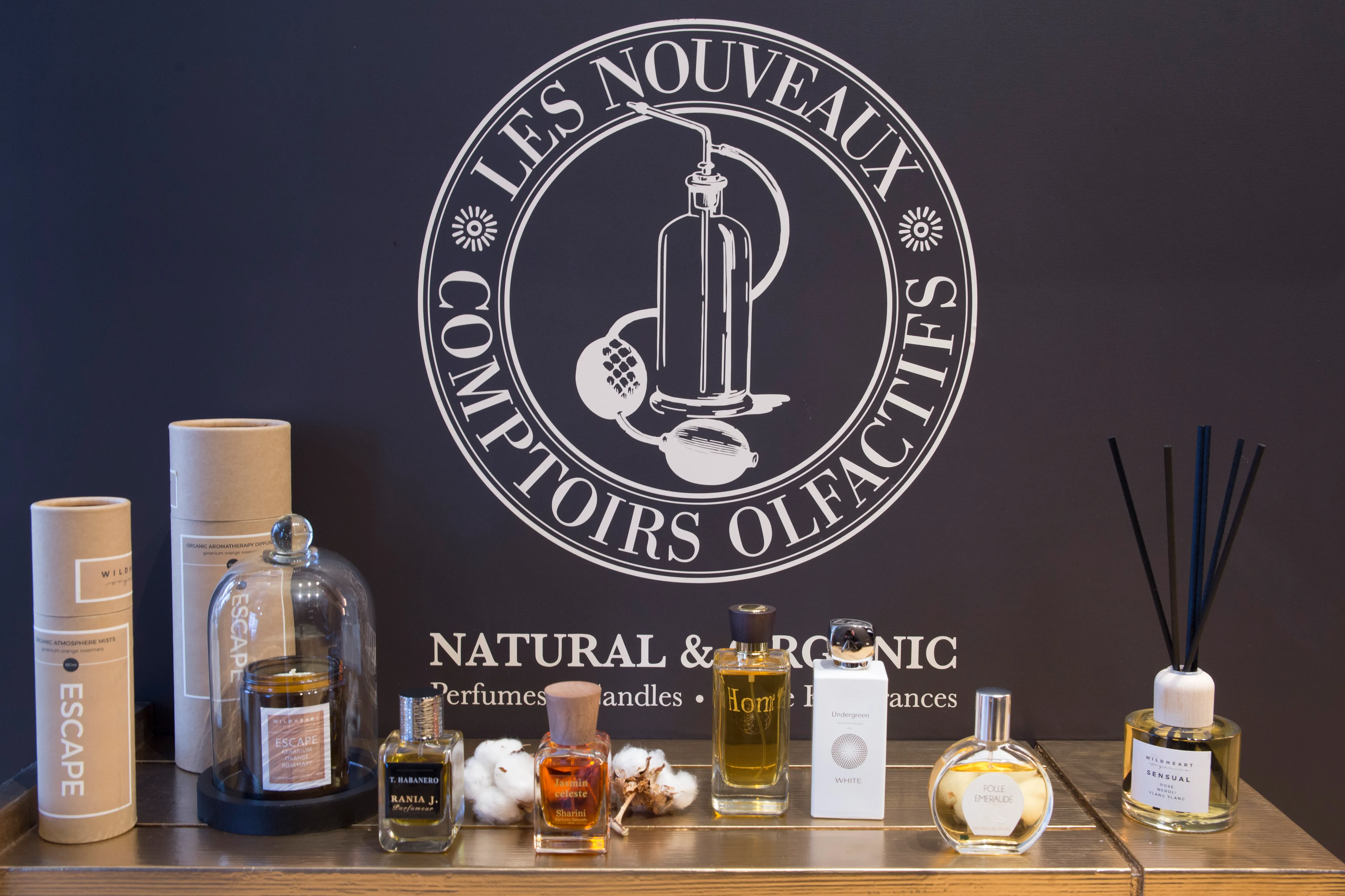 Une collection de parfums, bougies et diffuseurs devant un logo indiquant des parfums naturels et organiques.