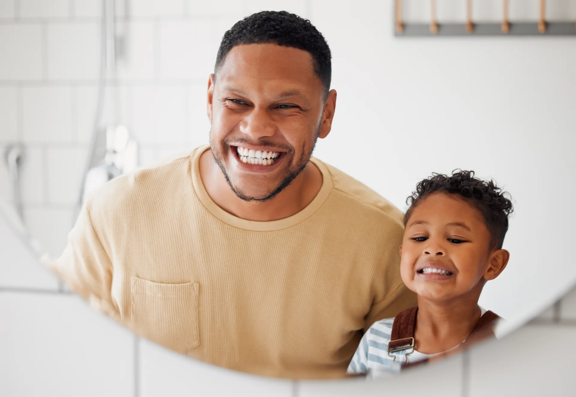 Smiling father and son looking at their reflection in a bathroom mirror.