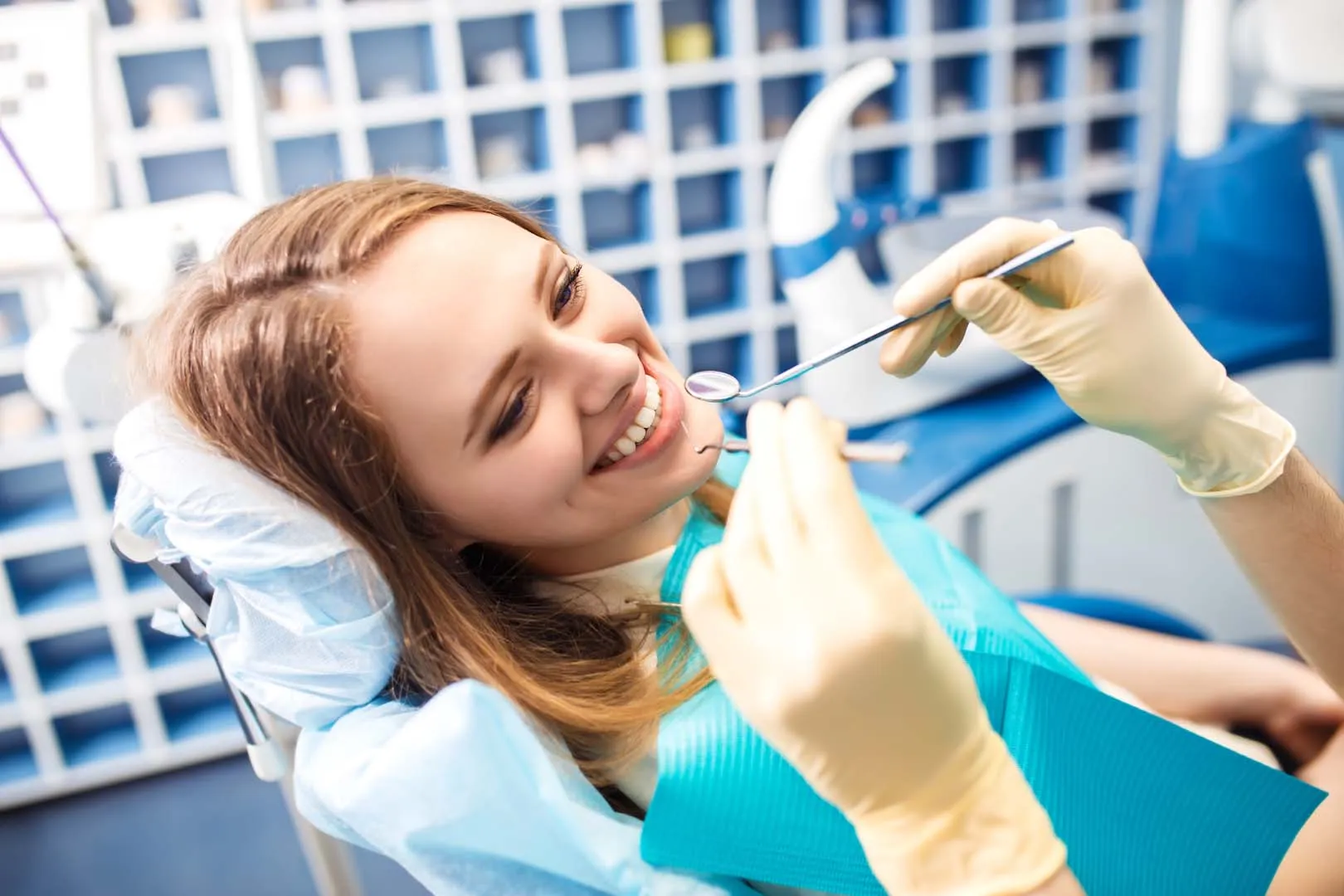 Smiling woman reclined in dental chair during dental checkup with dentist holding dental tools.