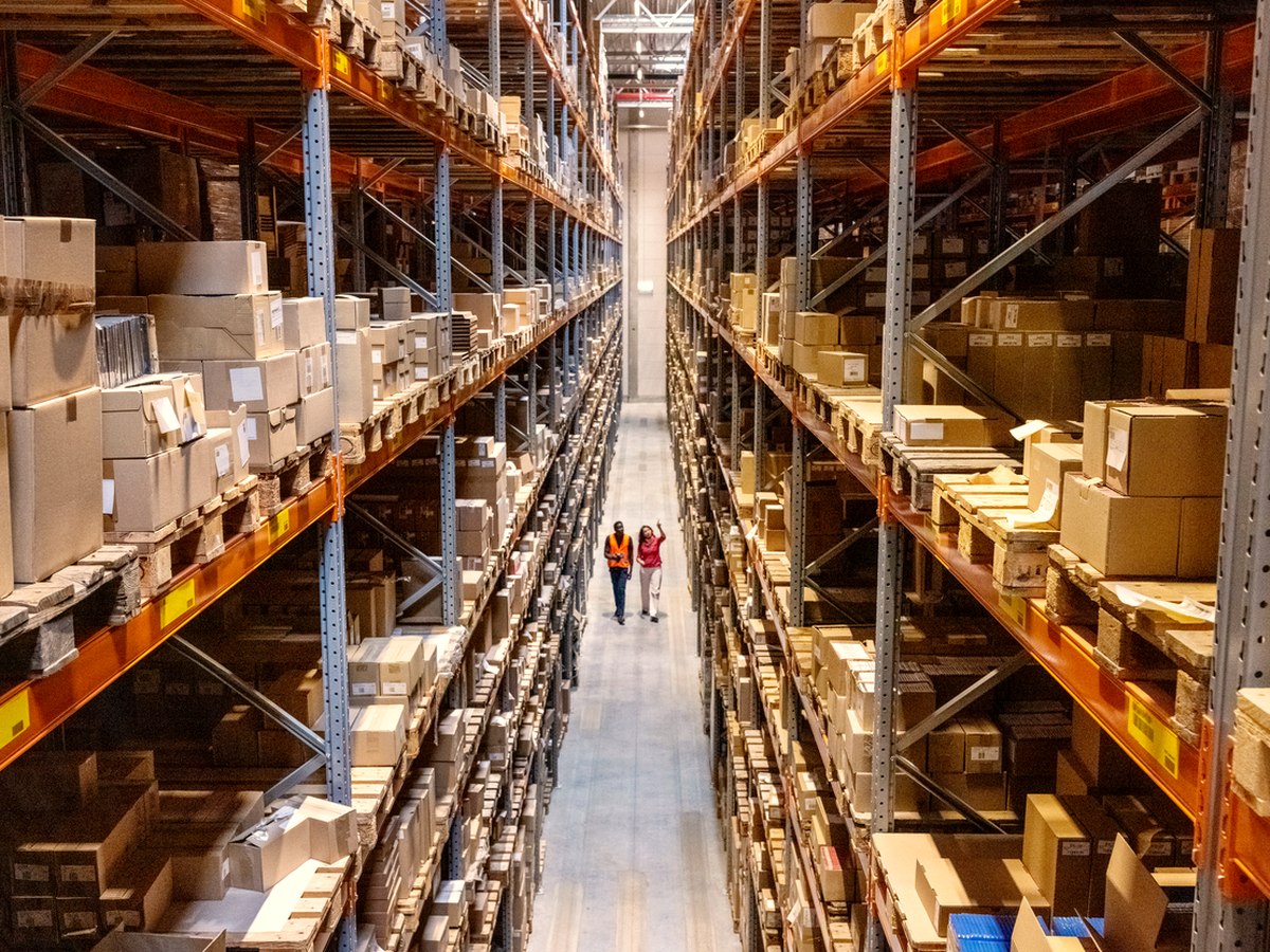 Two warehouse operators walking an aisle, reviewing inventory on a handheld