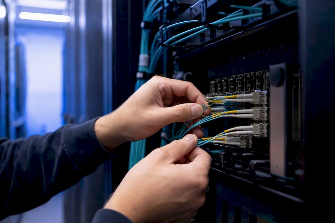 Hands plugging fiber optic cable in server rack
