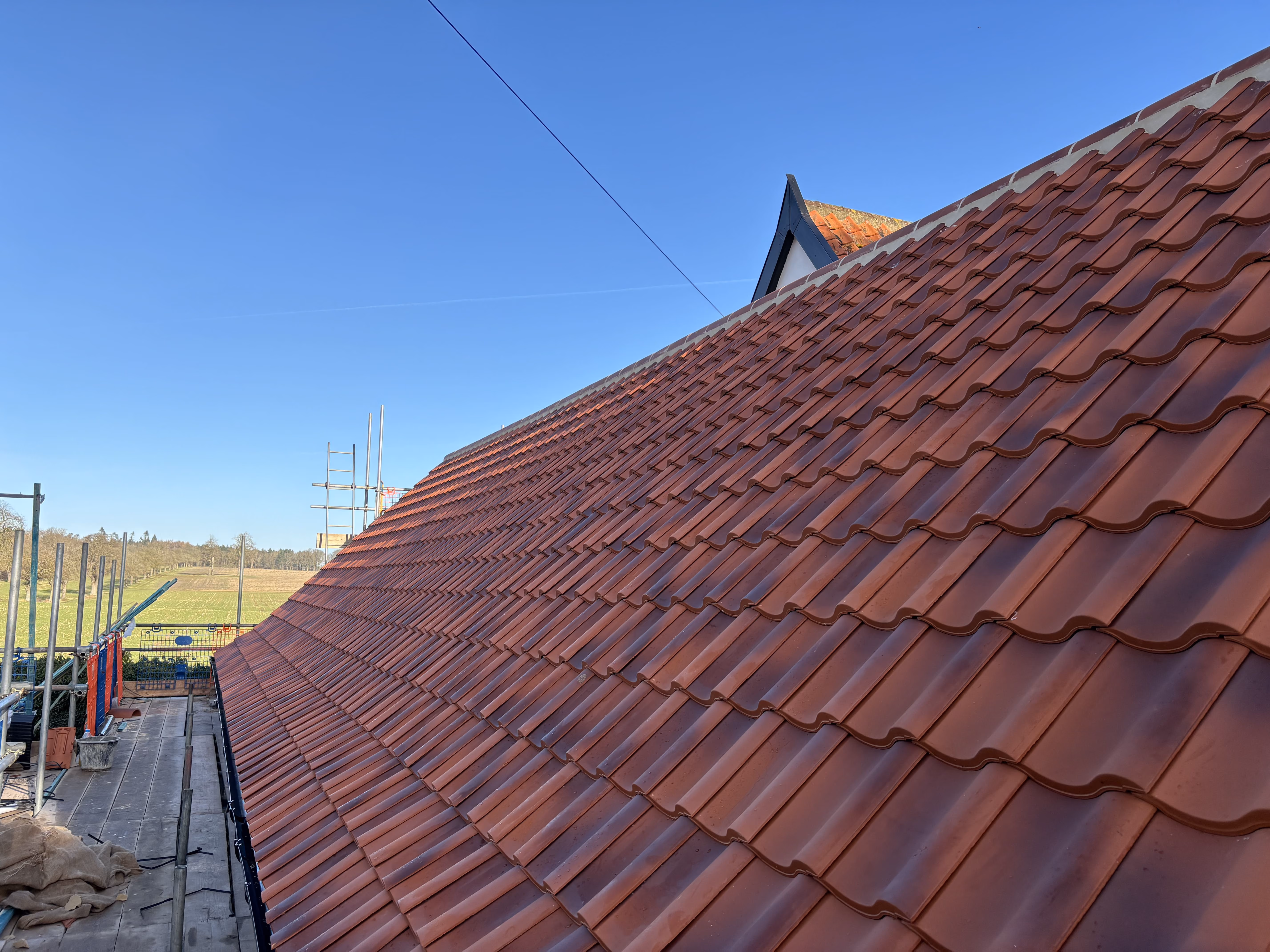 Close-up of a red-tiled roof under clear blue sky with construction scaffolding beside it.