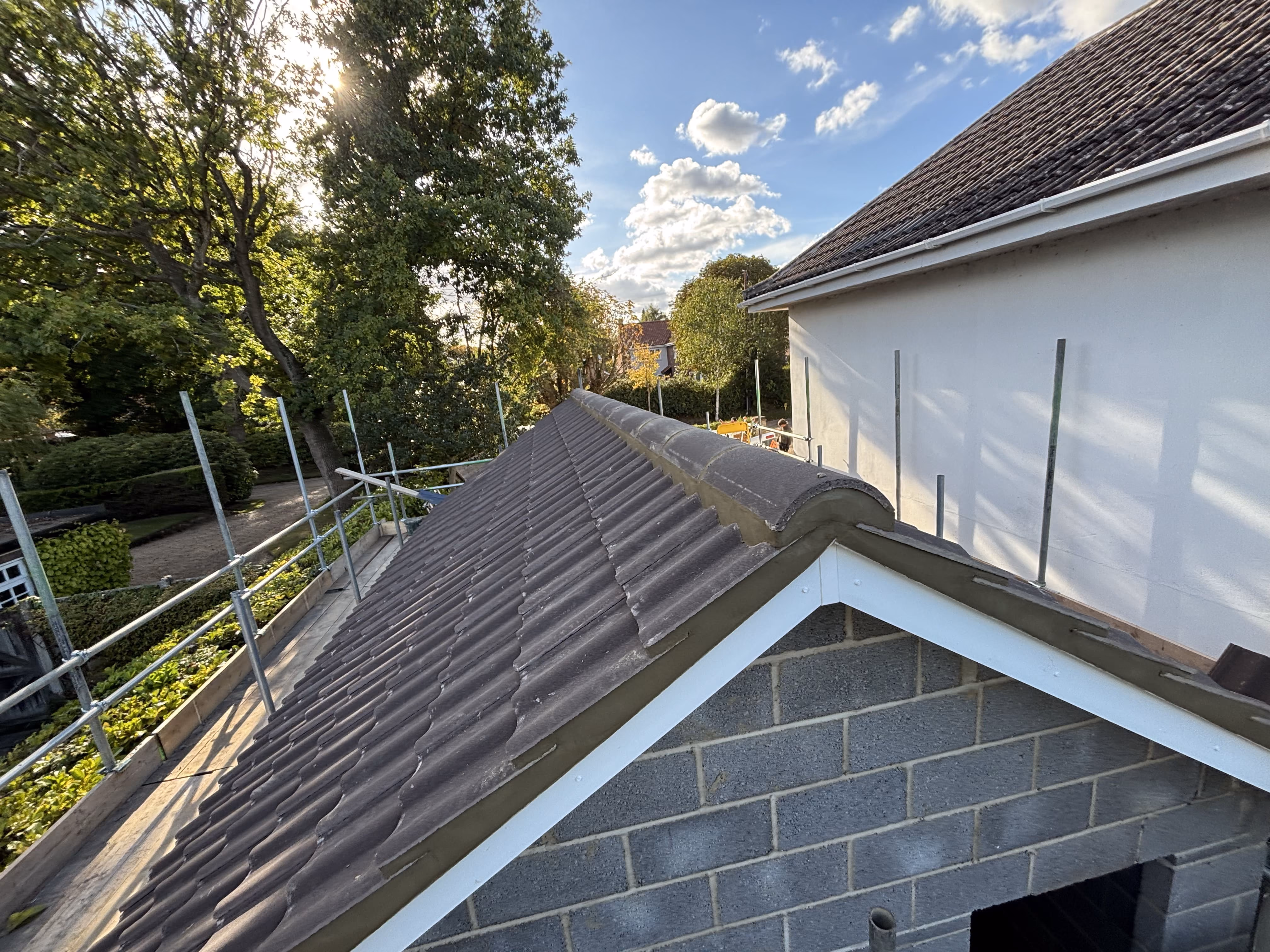 Newly tiled pitched roof on a small building under clear sky with scaffolding and green trees nearby.
