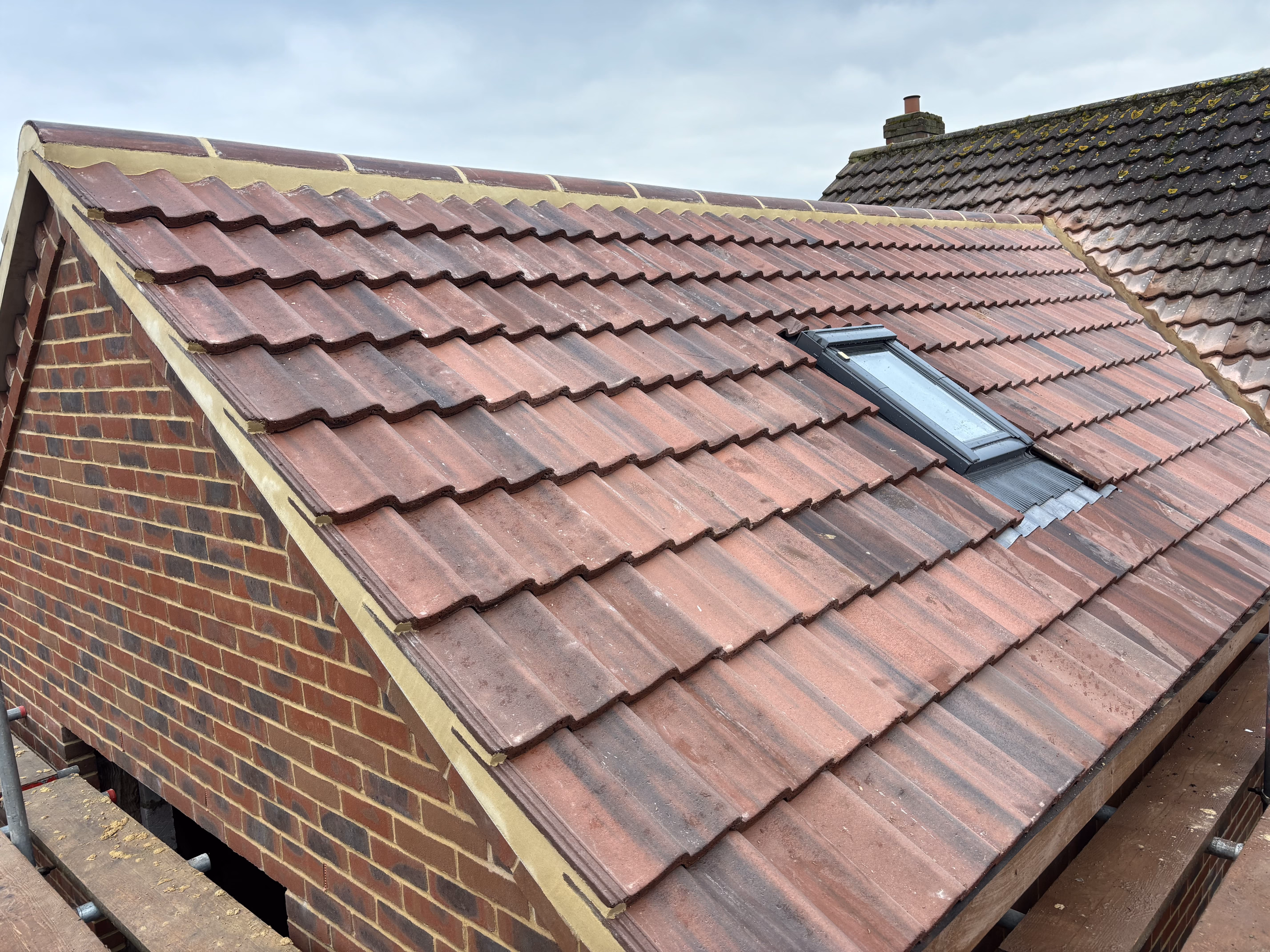 Brick house roof with red tiles and a small rectangular skylight under a cloudy sky.