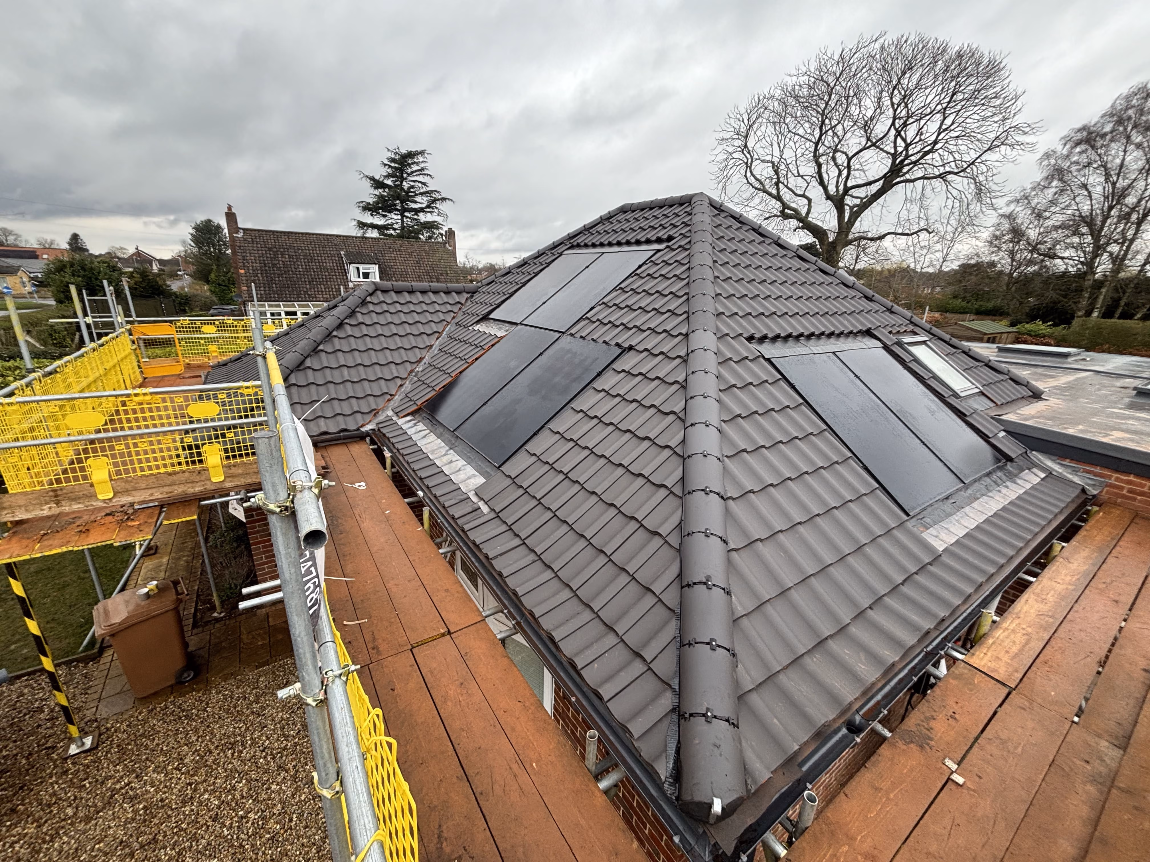 Roof with gray tiles and solar panels surrounded by yellow safety railings and scaffolding.