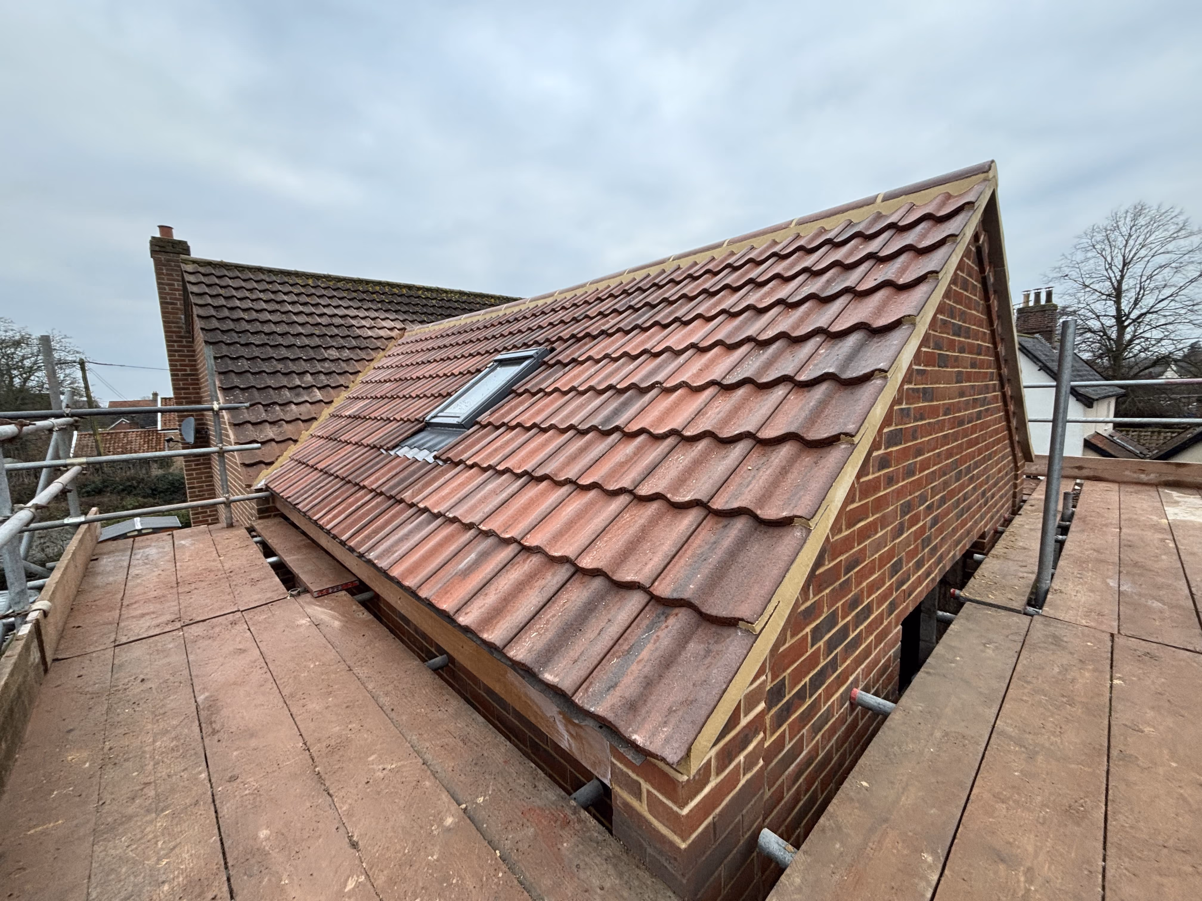 Newly tiled brick roof with a skylight and scaffolding platform around it on a cloudy day.