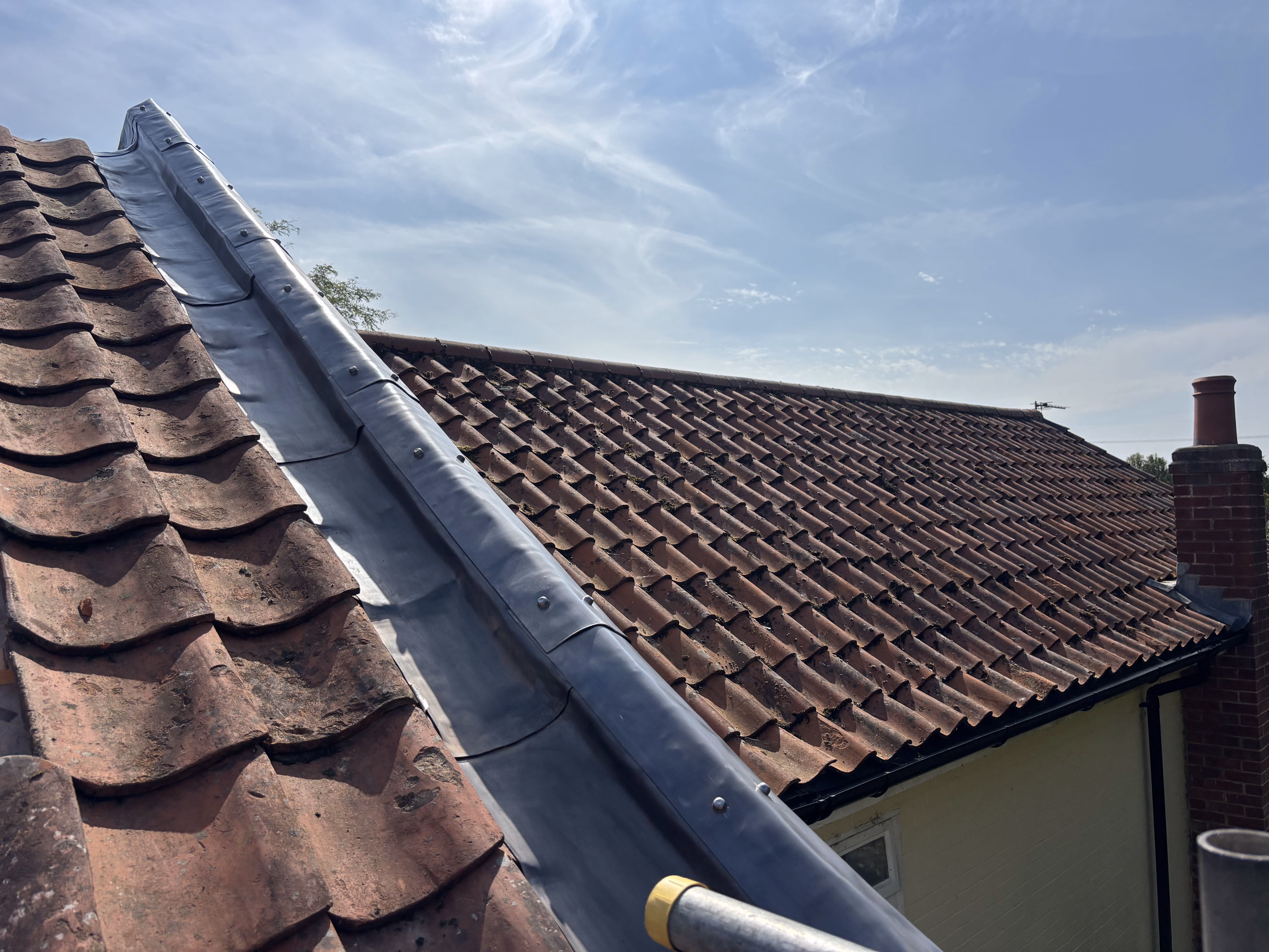 A tiled roof with a metal flashing strip running along the ridge under a partly cloudy sky.