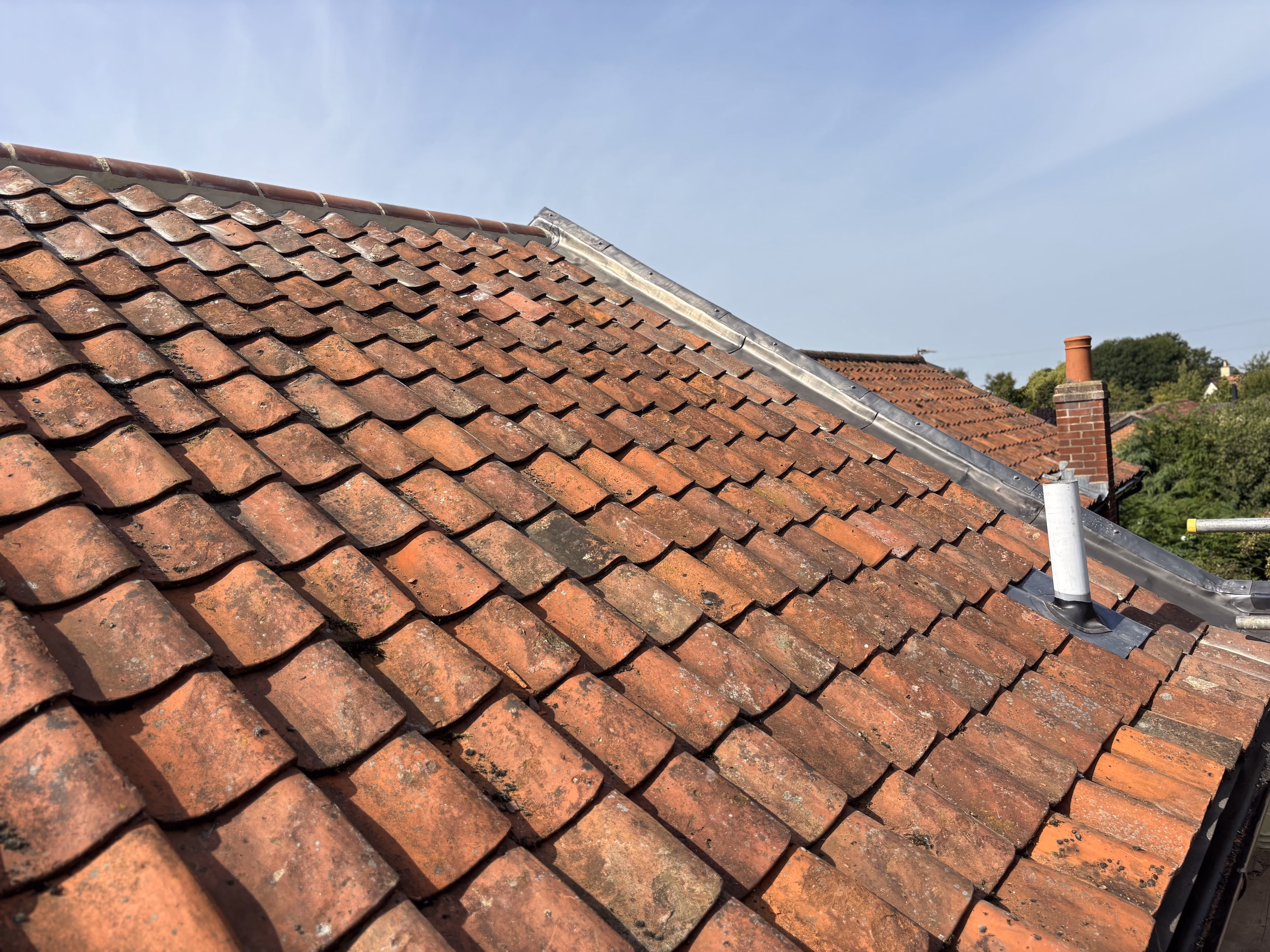 Close-up of a red clay tile roof with chimneys and a clear blue sky in the background.