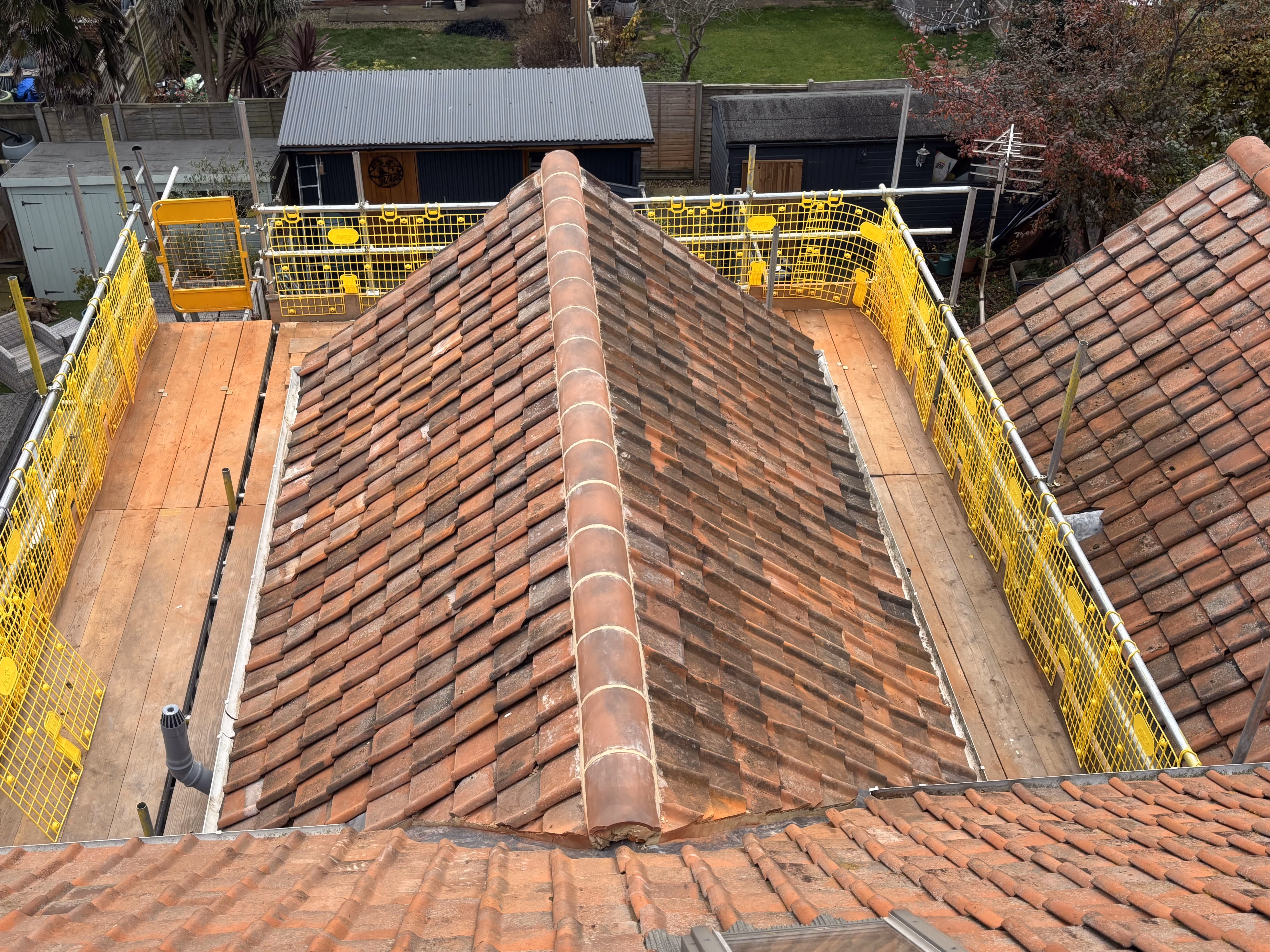 Roof with red tiles surrounded by yellow safety railings on wooden scaffolding.