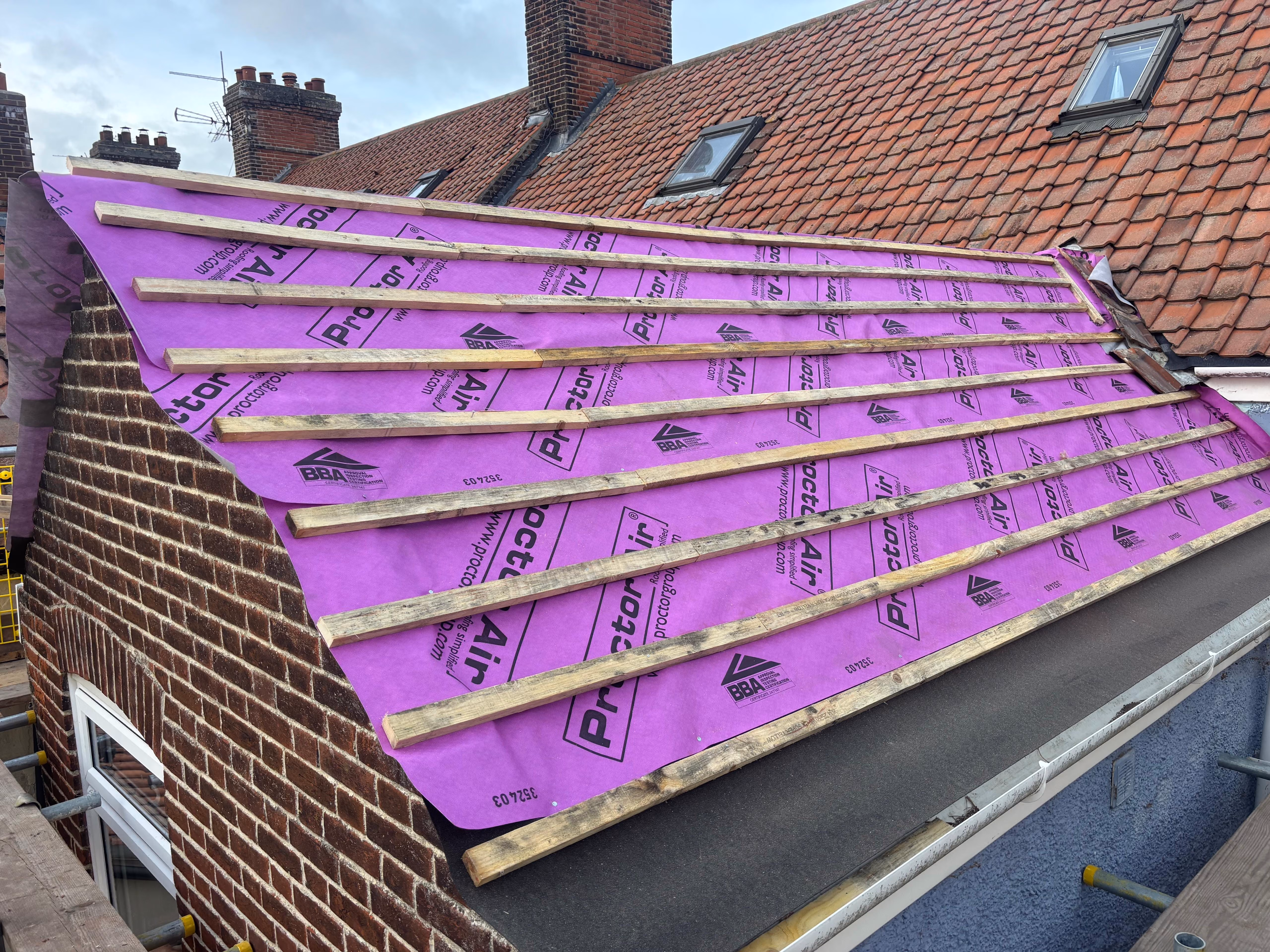 Roof under construction with a purple weatherproof membrane and wooden battens installed horizontally.