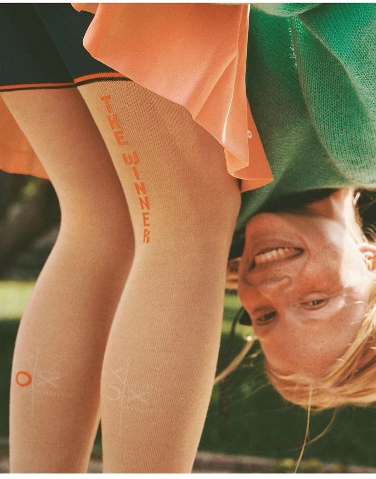 Person smiling upside down outdoors wearing beige tights with the words 'THE WINNER' in orange.