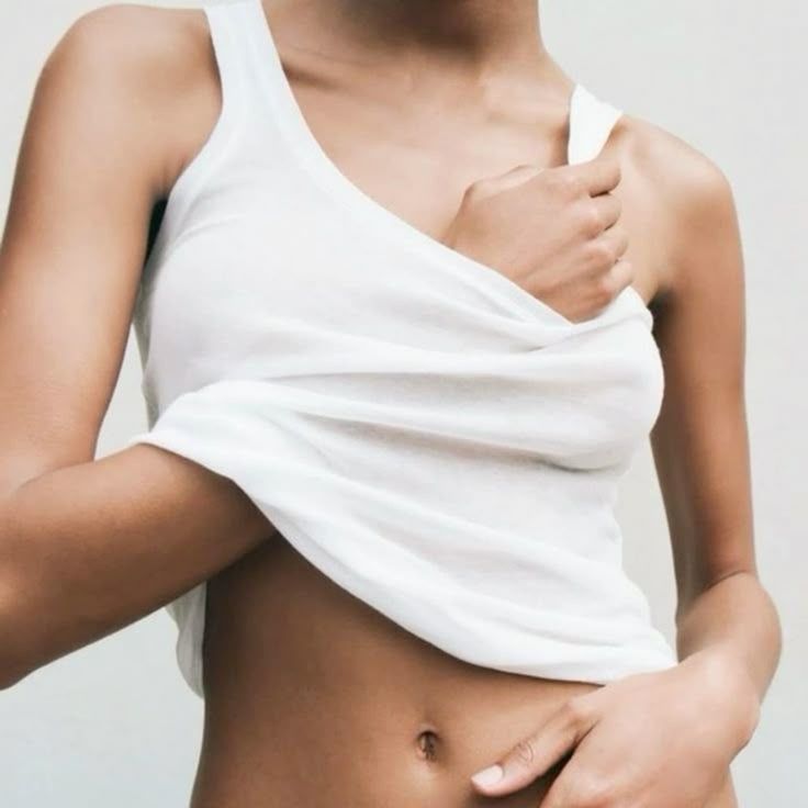Close-up of a person lifting their white tank top, exposing their midriff and belly button.