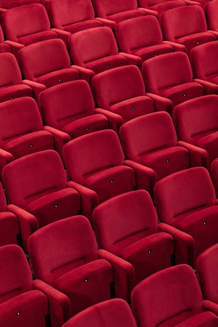 Rows of empty red velvet theater seats arranged in a pattern.