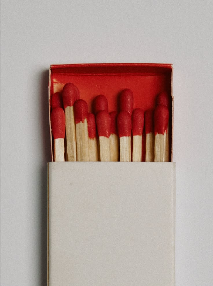 Open matchbox with wooden matches having red tips inside against a light background.