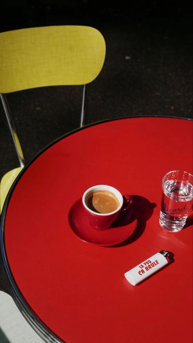 Red table with a red espresso cup, a glass of water, and a white lighter with red text.