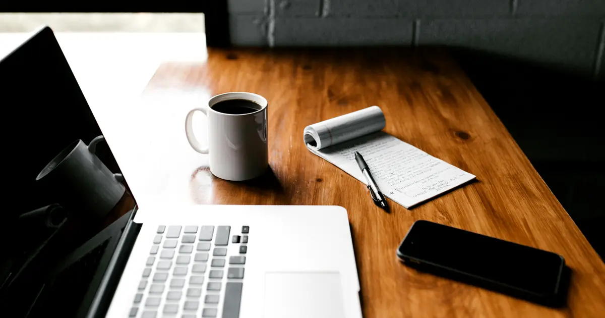 Laptop, coffee, and a handwritten notepad on a wooden desk while reviewing freight rate figures.